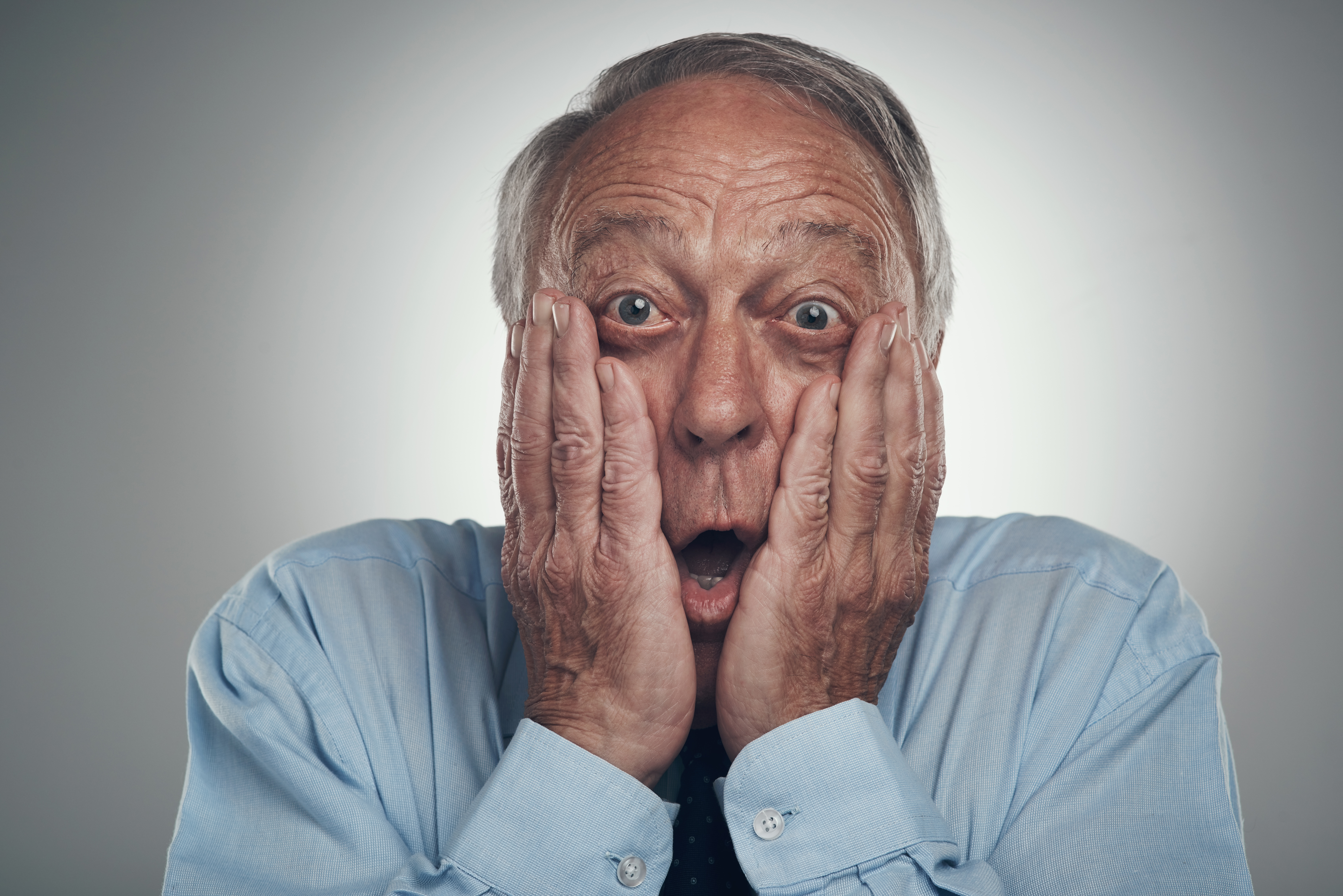 Shot of a senior businessman standing against a grey studio background with his face in his hands and looking shocked | Source: Getty Images