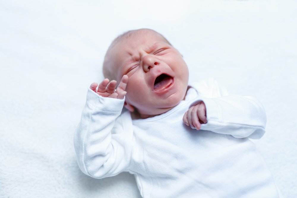 A baby cries while dressed in a white baby grow. | Photo: Shutterstock