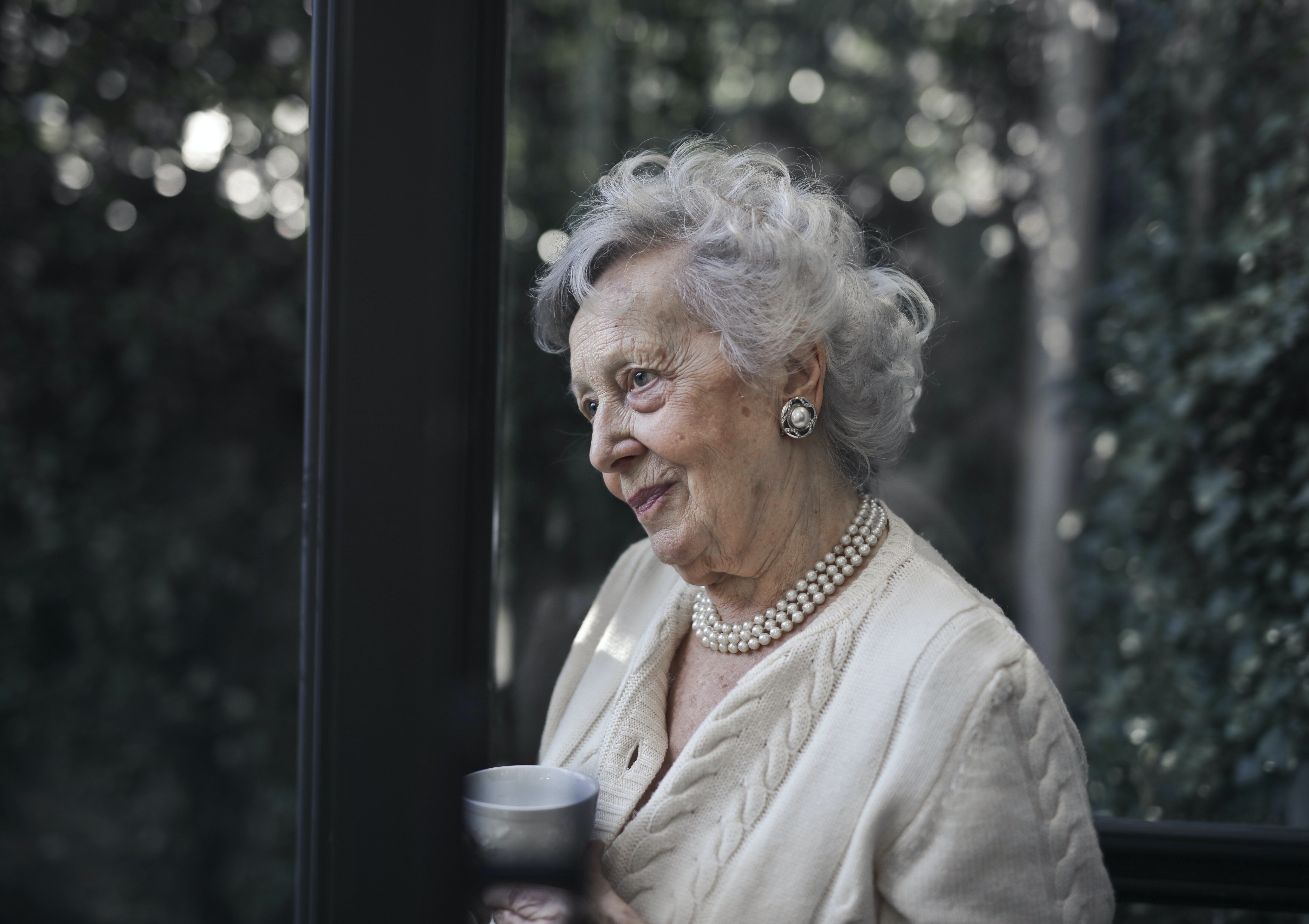 Una mujer anciana mira por la ventana. | Foto: Pexels