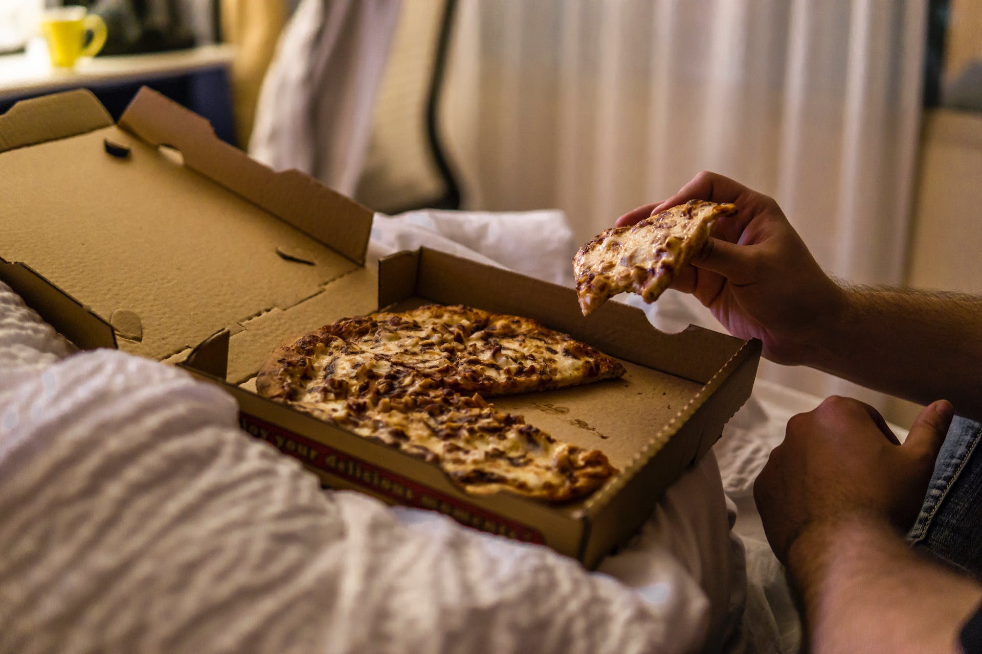 A man having pizza on his bed | Source: Pexels