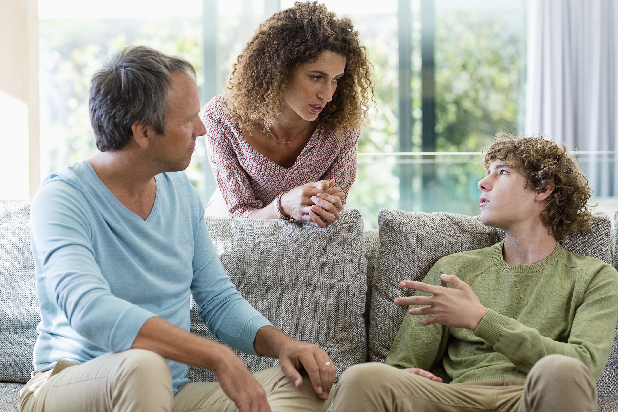 Eltern sprechen mit ihrem jugendlichen Sohn im Wohnzimmer | Quelle: Getty Images