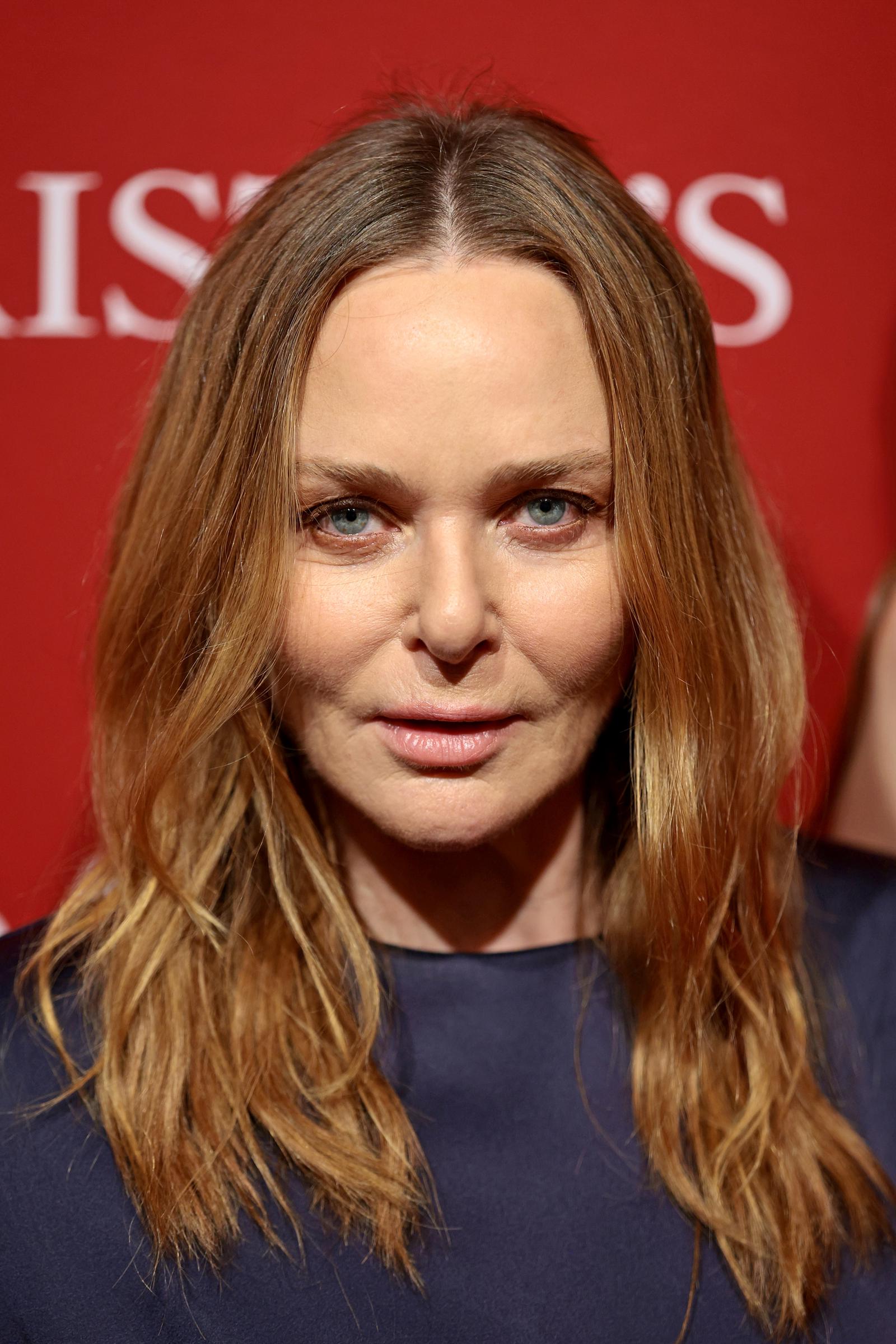 A close-up portrait of Stella shows her blue-grey eyes and centre-parted, honey-toned hair worn loose and natural, her expression cool and direct against the Christie's red backdrop.