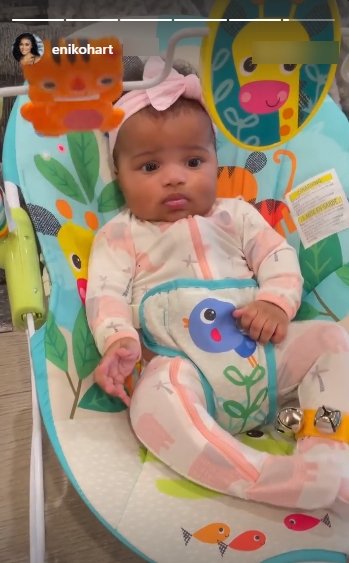 Kevin Hart's daughter, Kaori Mai, dressed in a colorful onesie and a pink bow while seated on a chair | Photo: Instagram/ enikohart