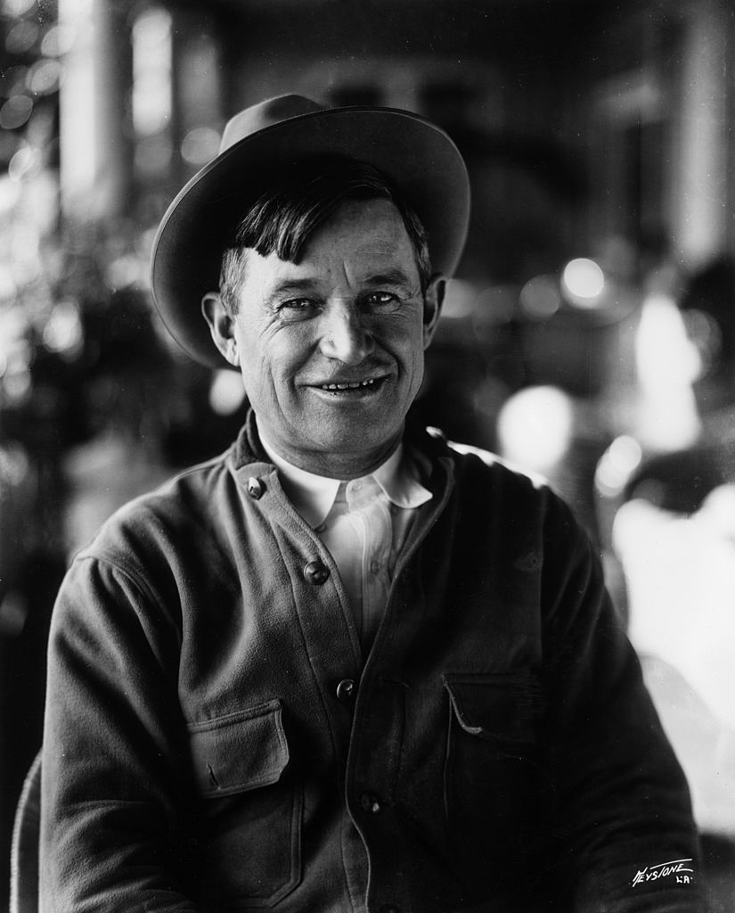 Portrait of American entertainer Will Rogers (1879-1935) sitting and smiling. He wears a hat and an overshirt. | Photo: Getty Images