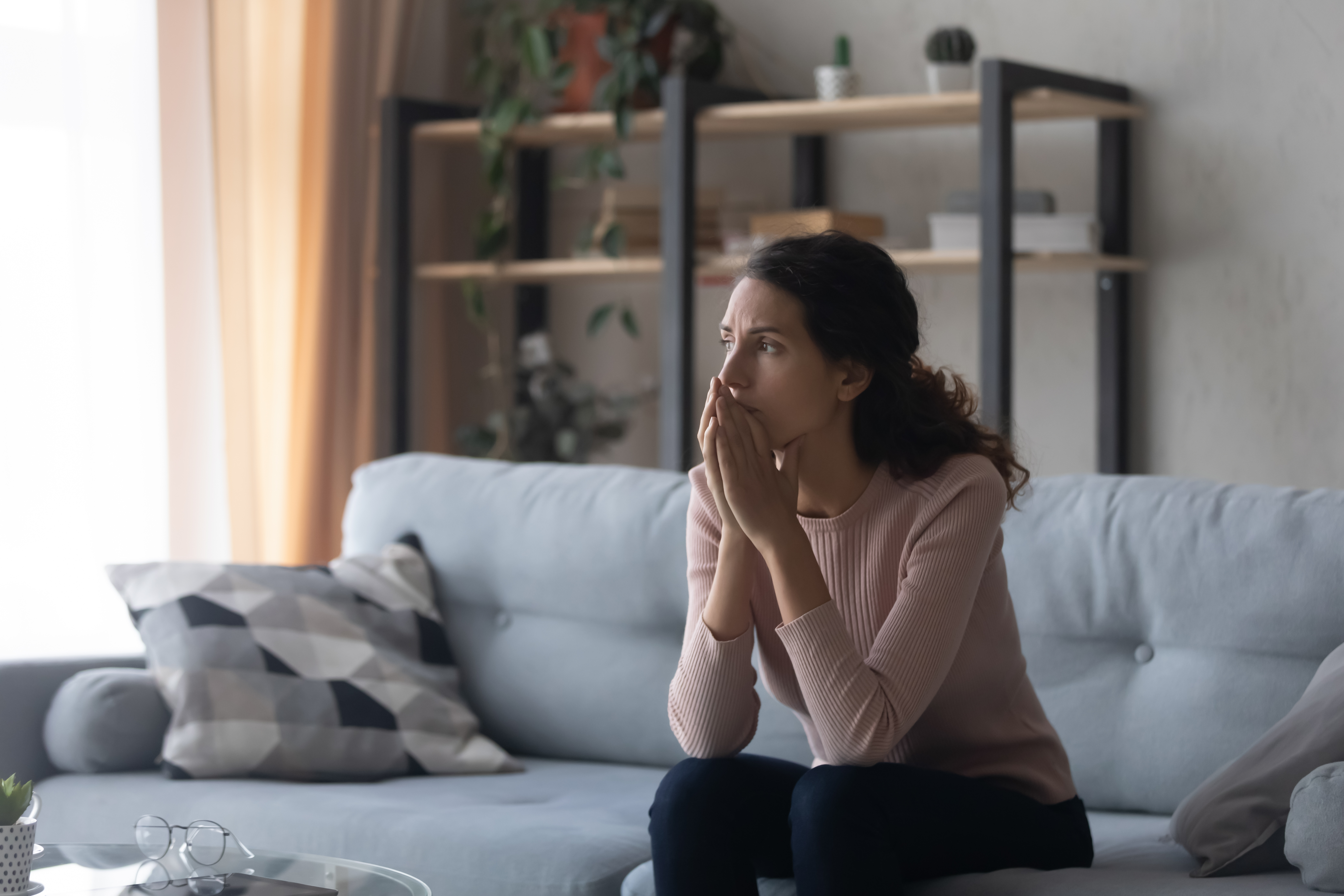 A young woman, visibly stressed, sitting alone on a couch | Source: Shutterstock