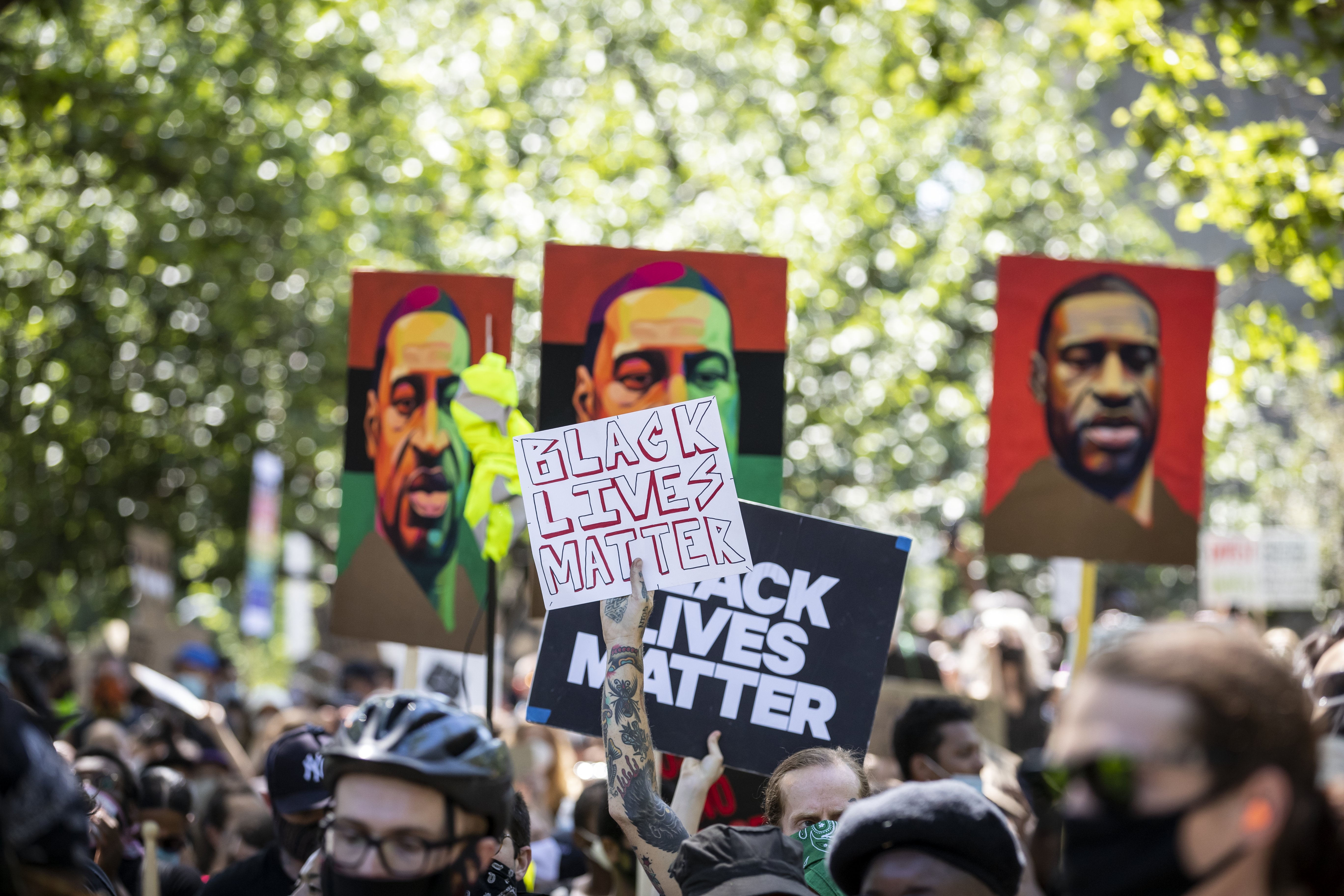 A protester with tattoos holds a sign that says, "Black Lives Matter" with three painted portraits of George Floyd at the Brooklyn Borough of New York on June 19, 2020 | Photo Getty Images