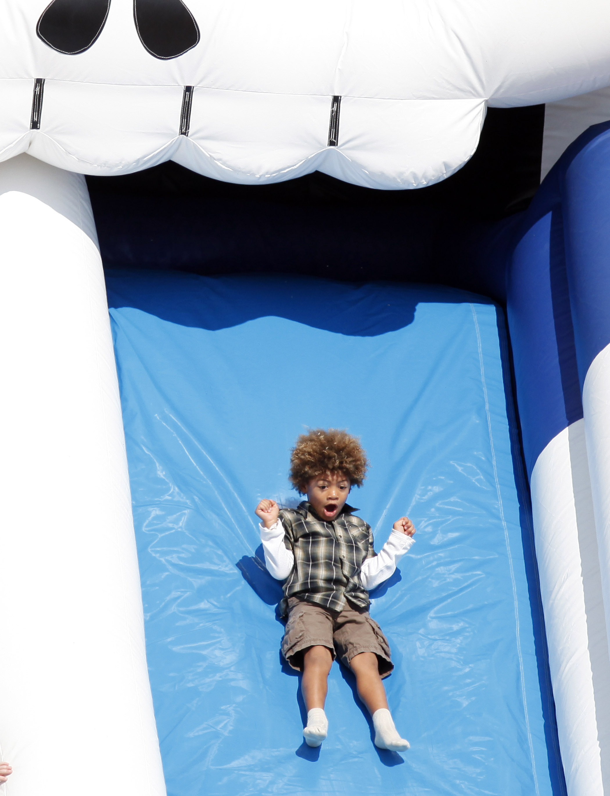 Caught mid-slide, Henry Samuel rides a wave of pure joy, his wide-eyed surprise and lifted fists capturing the thrill of the moment as he zips down a bright blue inflatable at Mr Bones Pumpkin Patch in West Hollywood.