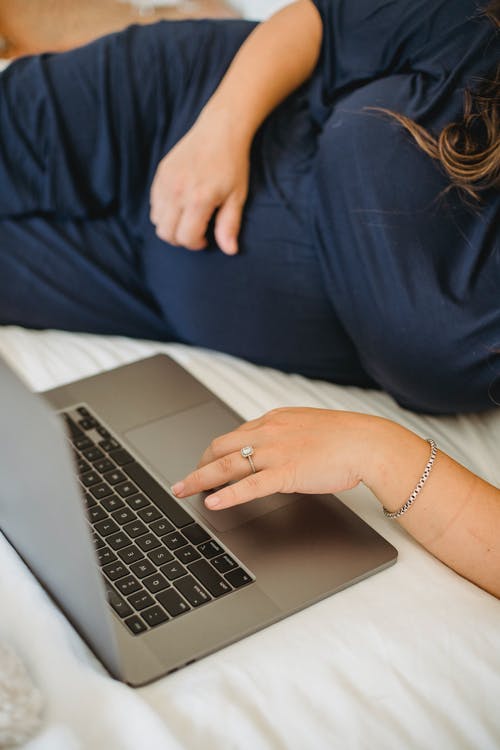 Mujer embarazada trabajando frente al ordenador recostada en su cama. | Foto: Pexels