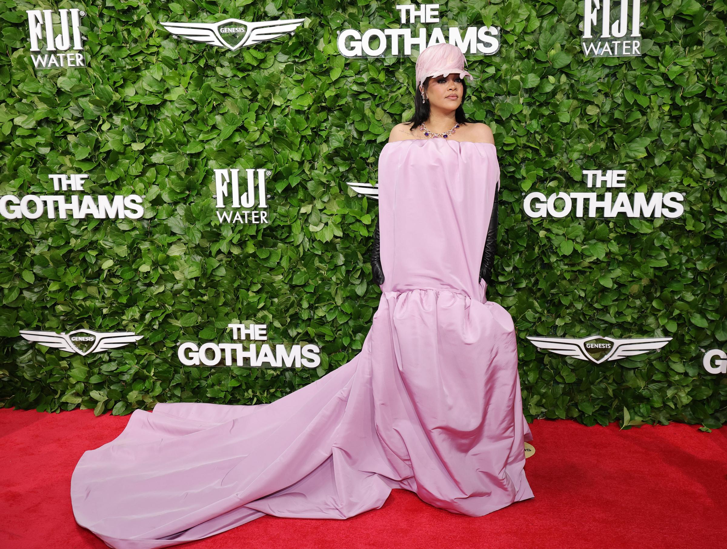 Rihanna stands alone in front of the Gotham Awards step-and-repeat, letting her dramatic train and matching accessories take center stage in a commanding red carpet moment.