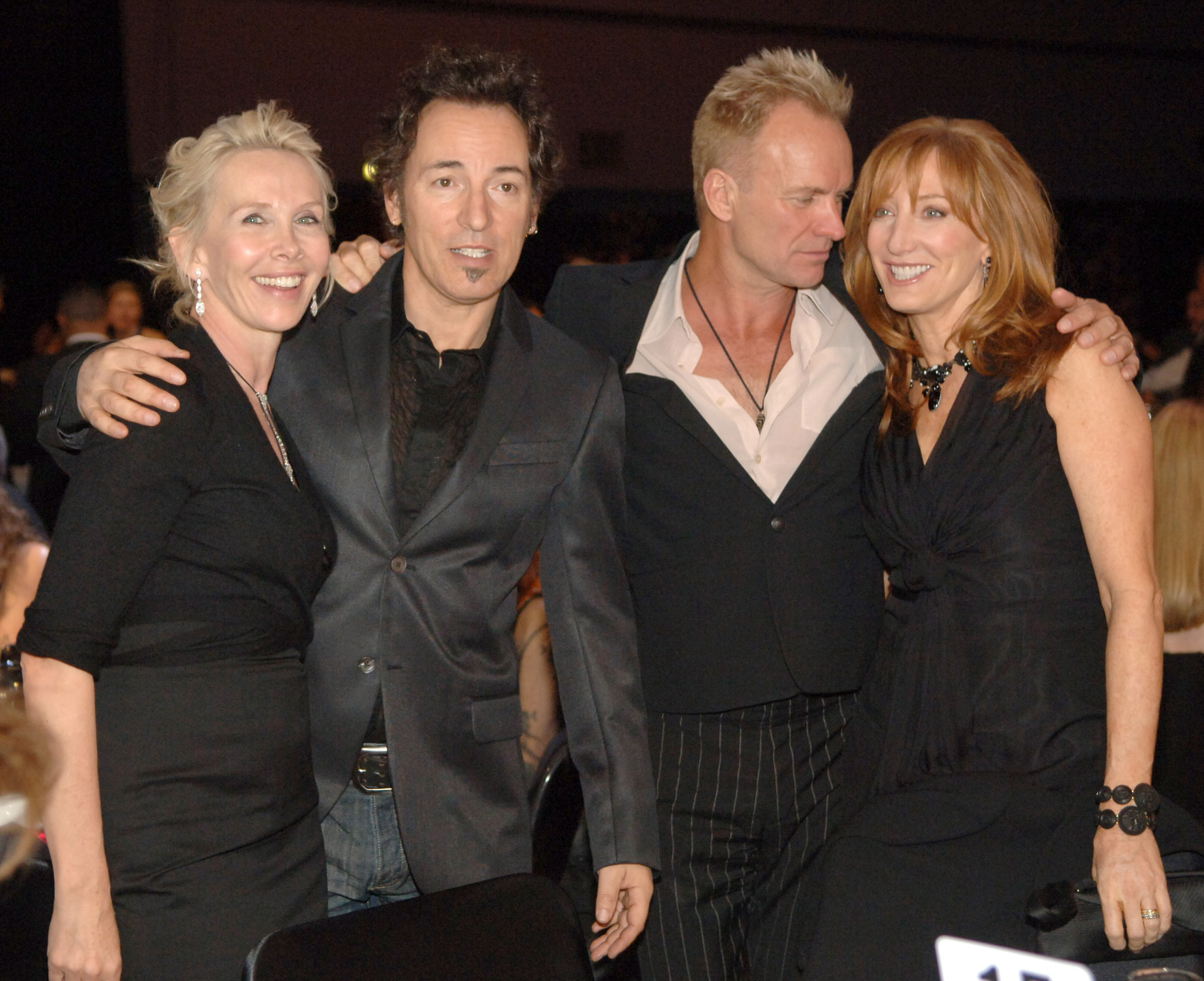 Backstage at the 2006 MusiCares Person of the Year event honoring James Taylor, Trudie Styler joins Bruce Springsteen, Sting, and Patti Scialfa for a group photo. The four share a warm moment behind the scenes.