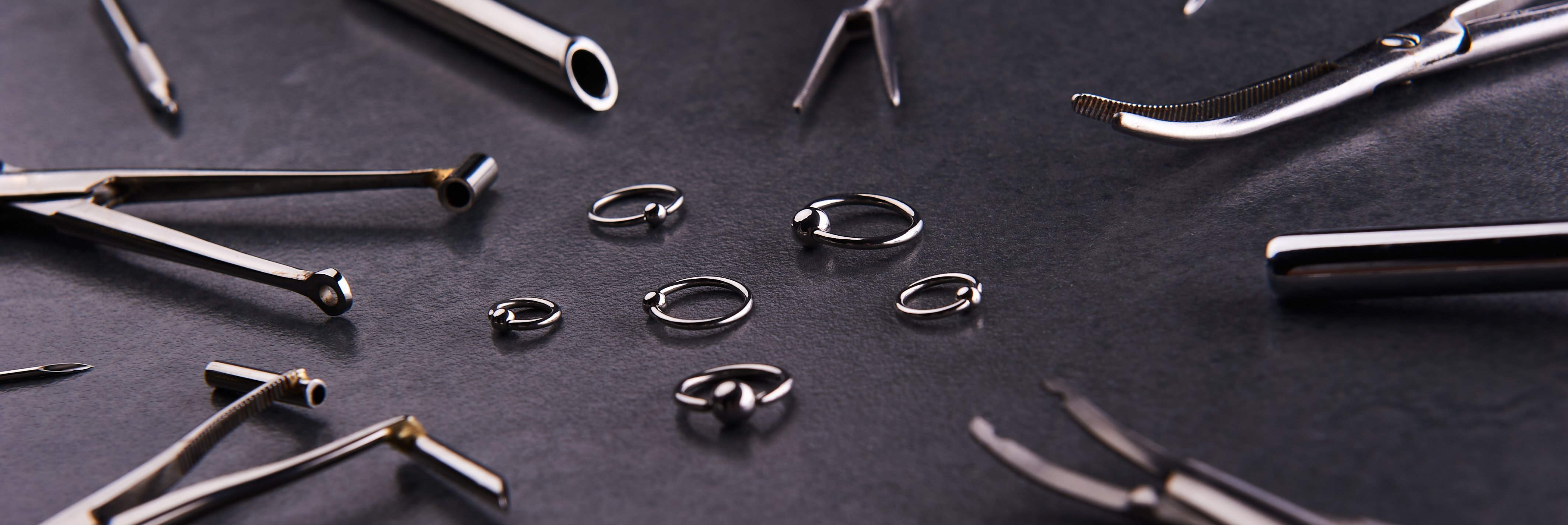 Piercing-Instrument, Clips, die neben Ohrringe auf schwarzem Hintergrund liegen. | Foto von: Sychov Serhii via Shutterstock