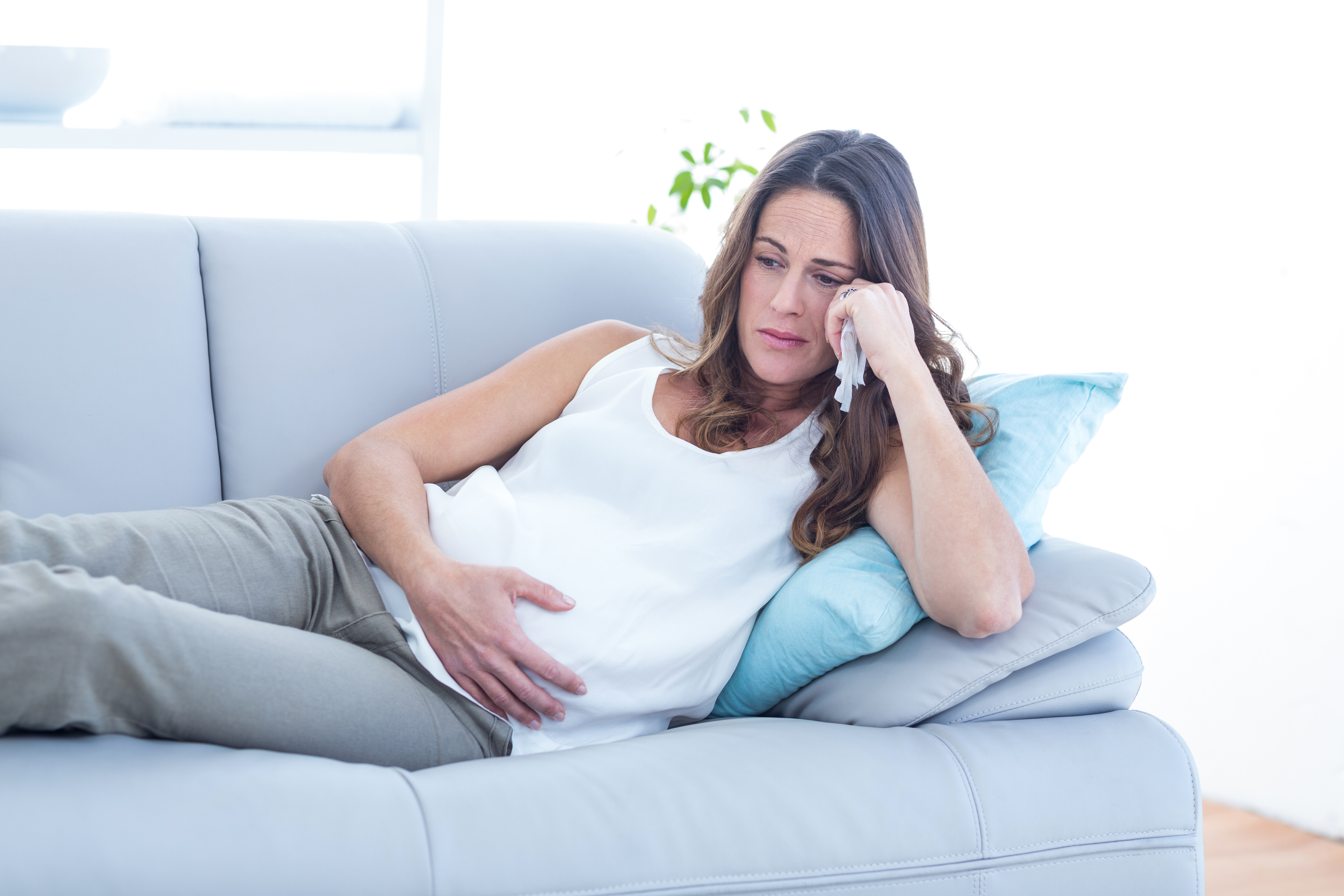 A pregnant woman sitting on a couch looking sad | Source: Shutterstock