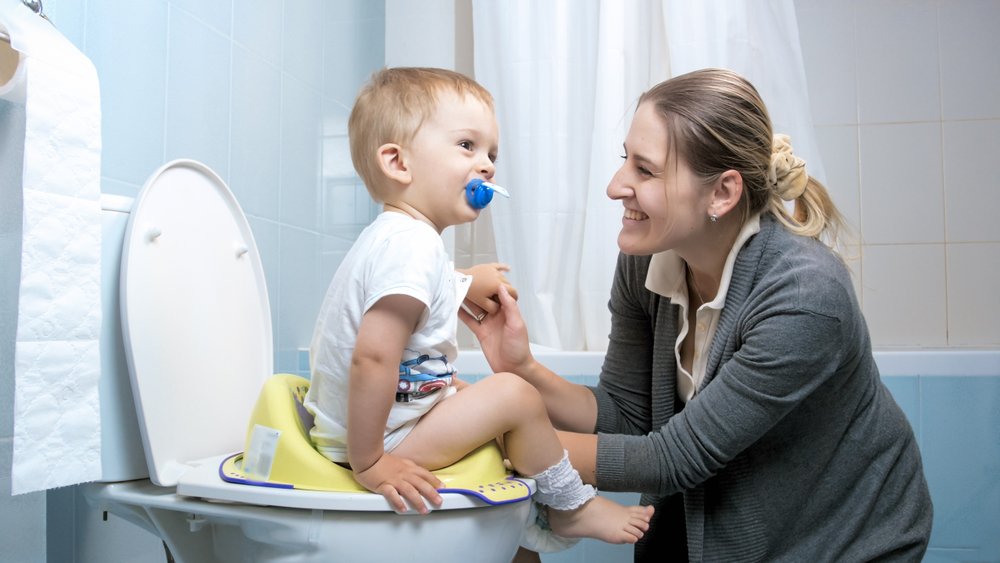 A young mother talking to her toddler son who is using his potty | Photo: Shutterstock
