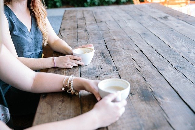 Women sitting down drinking cups of coffee on a bench | Photo: Pixabay