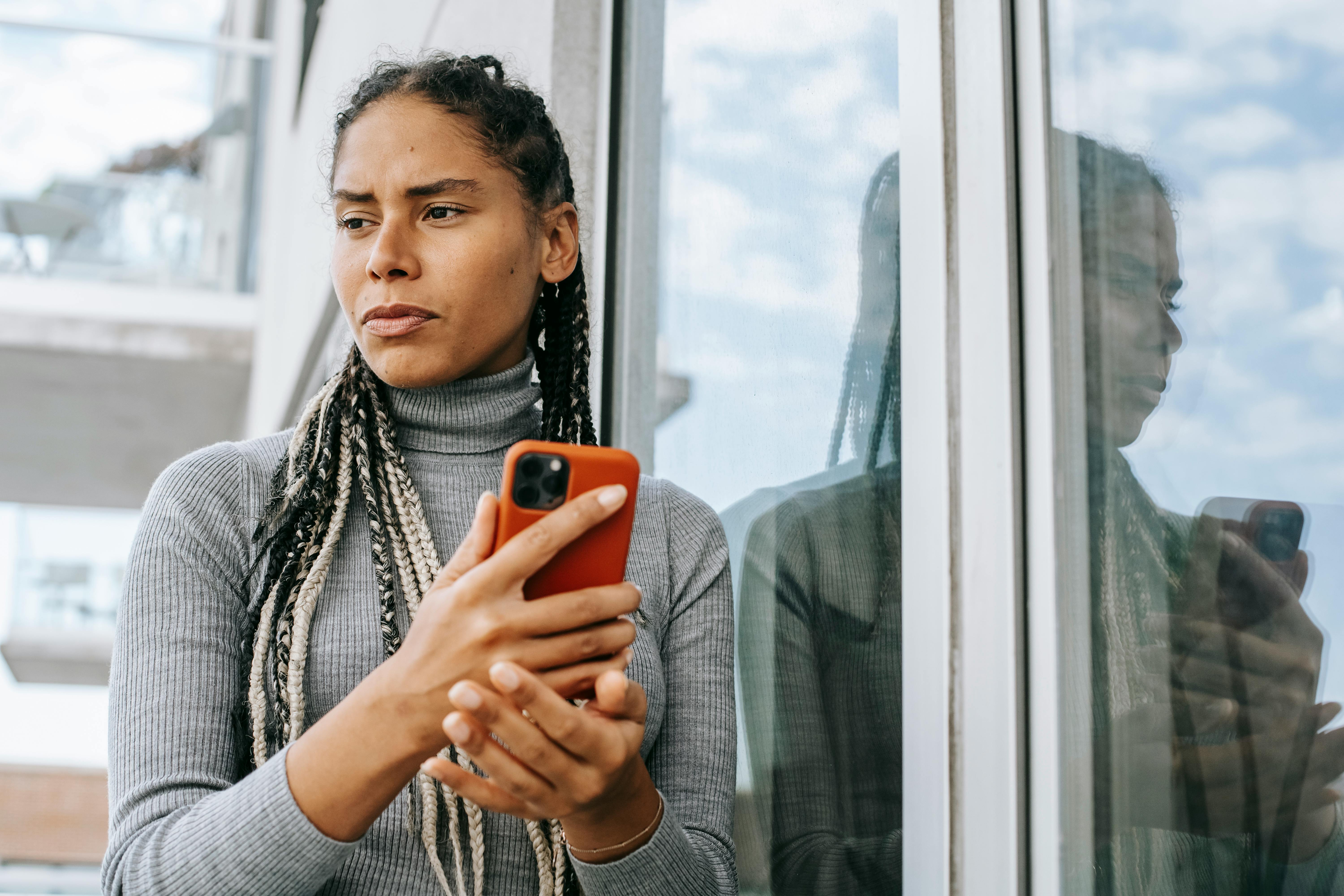 A woman looking to the side while contemplating something with her phone in hand | Source: Pexels