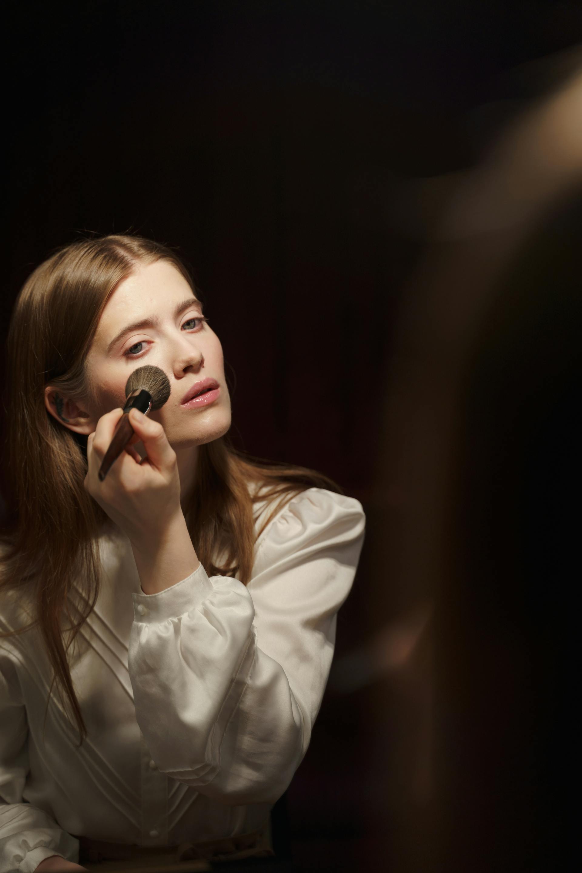 A woman applying makeup while looking in the mirror | Source: Pexels