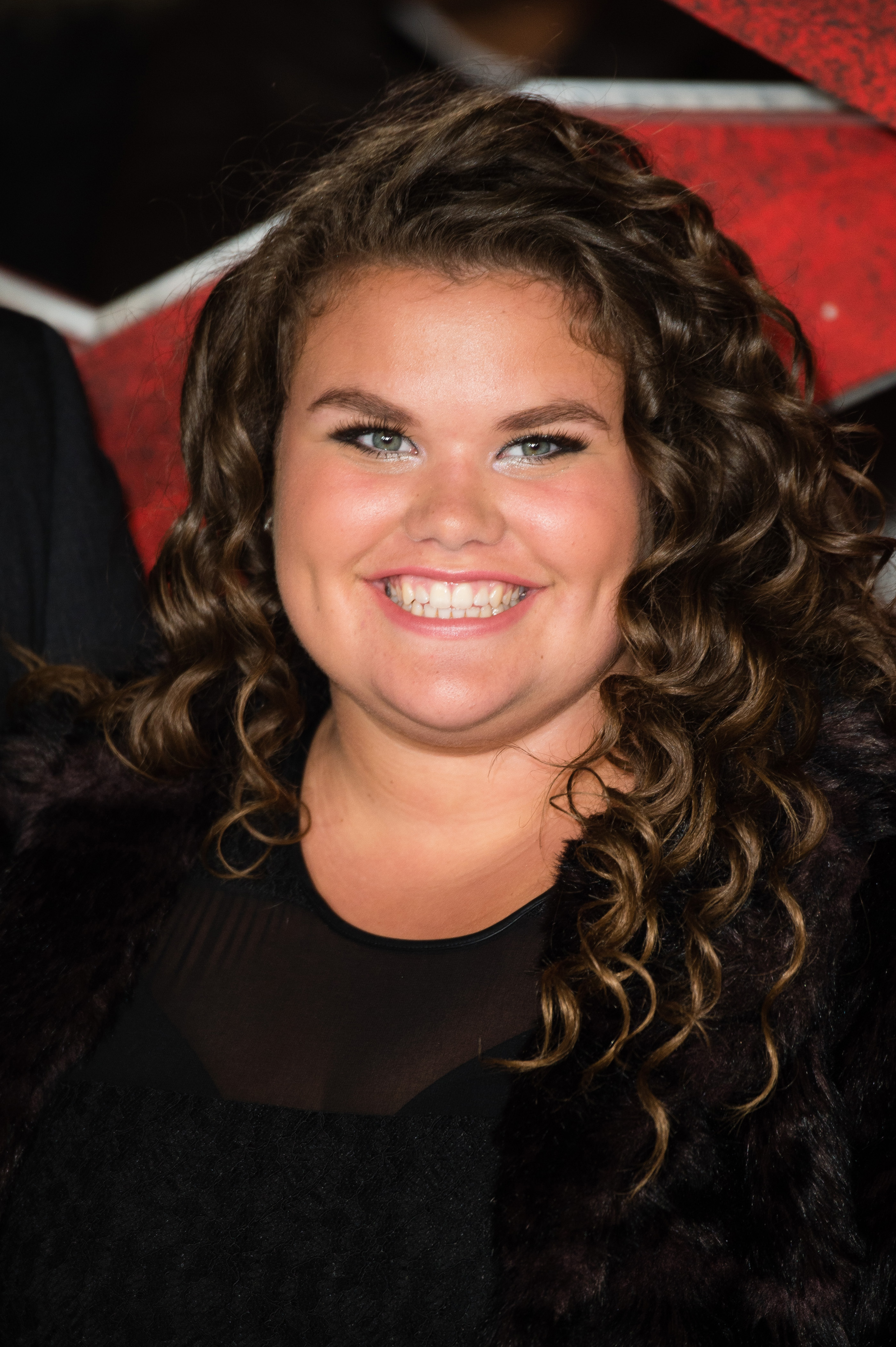 A teenage Amy Tapper beams at the camera, her long dark curls tumbling past her shoulders, at the European premiere of "xXx: Return of Xander Cage" in London, on 10 January 2017. She is dressed in a black fur-trimmed coat over a sheer top, and a standout makeup look with bold smoky eye.