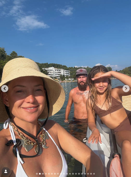 Family members gathered in the water near the shore during the European getaway, with a tree-lined coast behind them. The swimwear and seaside setting establish the warm-weather trip that later frames Goldie Hawn's appearance in the family video. | Source: Instagram/katehudson