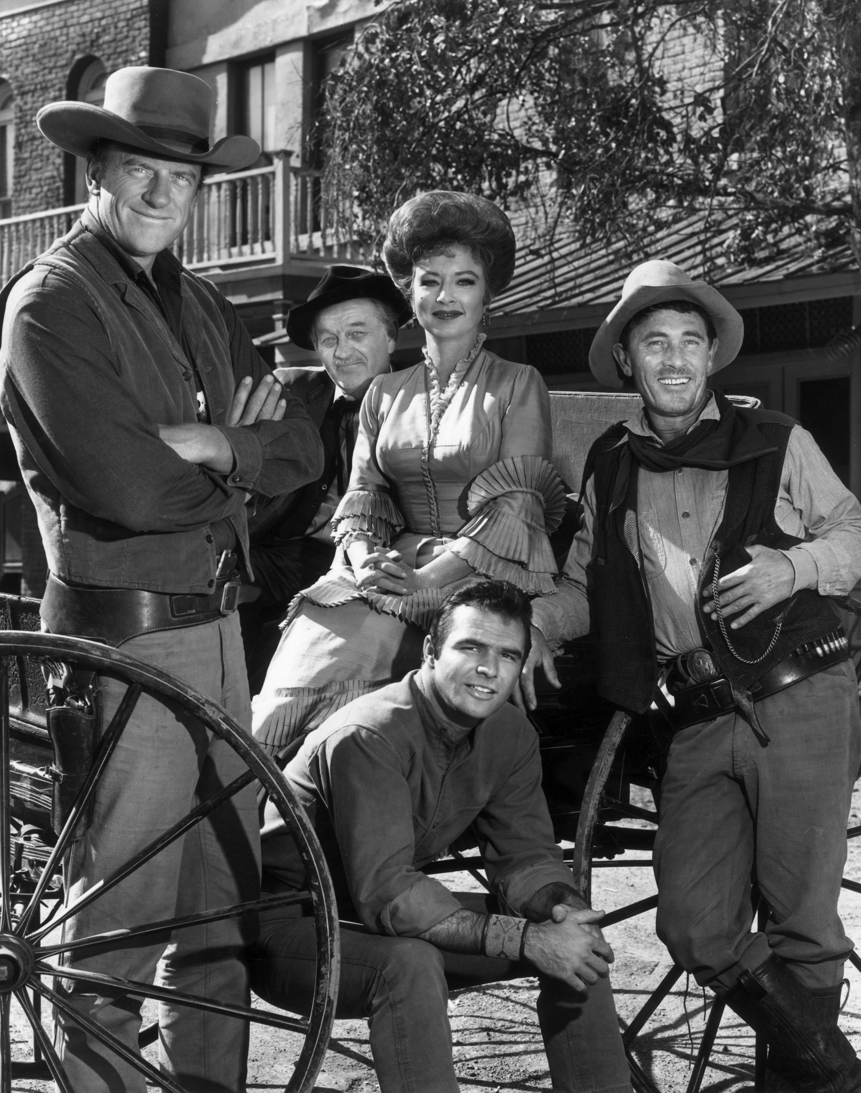 The cast of 'Gunsmoke' poses around a wagon in a promotional portrait for the Western television series. L-R: Actors James Arness, Milburn Stone, Amanda Blake, Ken Curtis and Burt Reynolds (seated). | Source: Getty Images