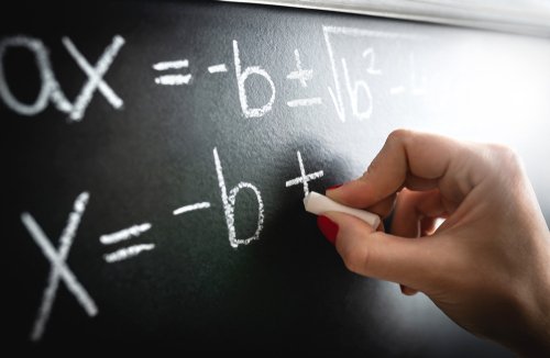 A teacher writing a math equation on a black board. | Source: Shutterstock