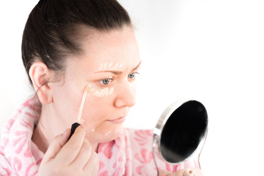 Mujer aplicando base correctora en el contorno de sus ojos. | Foto: Shutterstock