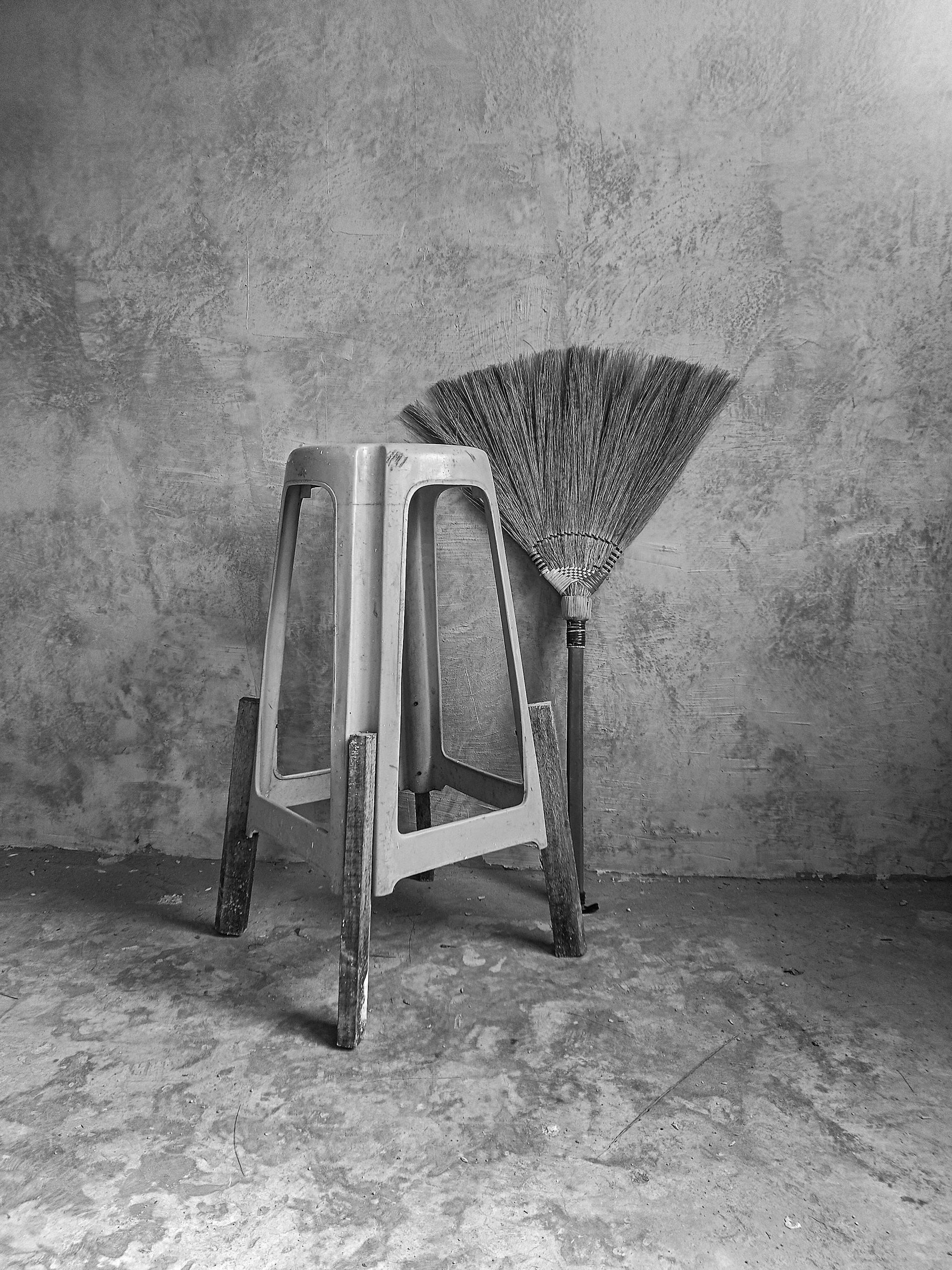 A grayscale photo of a stool and a broom lying next to the wall in a room | Source: Pexels