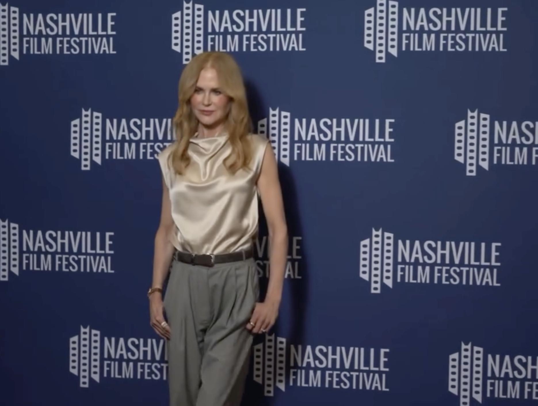 On the red carpet at the Nashville Film Festival, Nicole Kidman stuns in a champagne silk blouse and high-waisted trousers, offering a poised smile against the branded blue backdrop. | Source: Instagram/nicolekidman