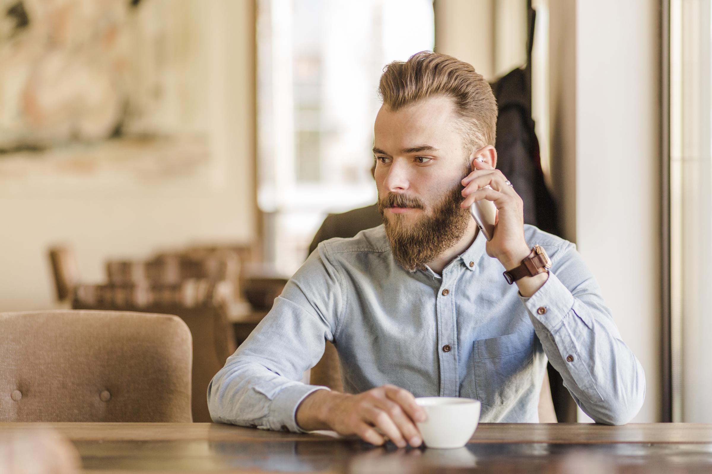 A man sitting at the table with a cup and his phone | Source: Freepik