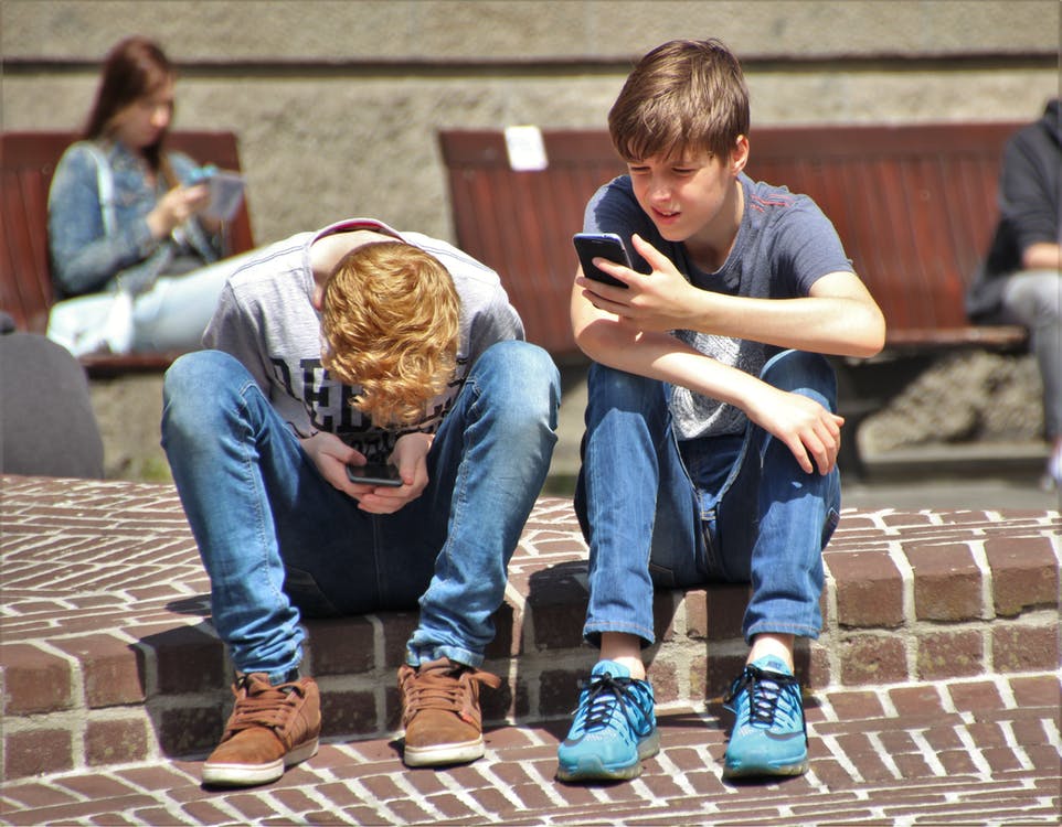 Dos adolescentes sentados en unos escalones mientras miran sus teléfonos celulares. | Foto: Pexels