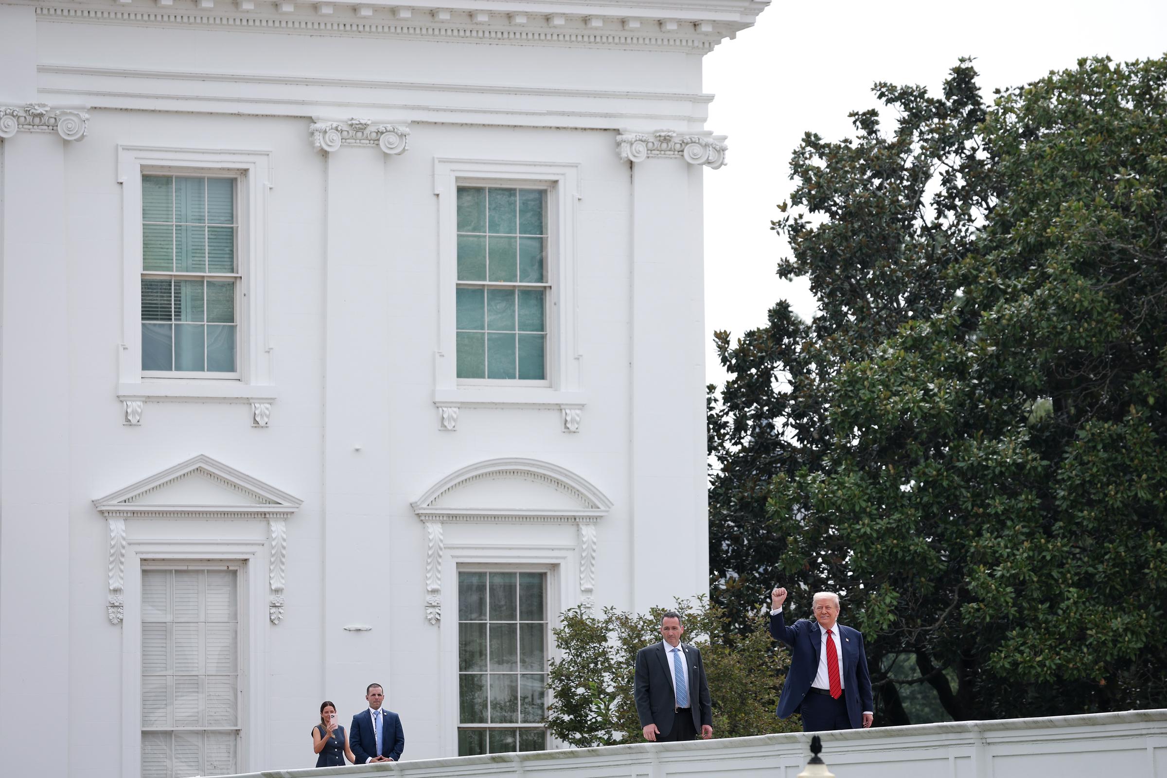 Donald Trump appears to wave while speaking to reporters during a rooftop tour of the White House's West Wing in Washington, D.C., joined by aides and security staff.