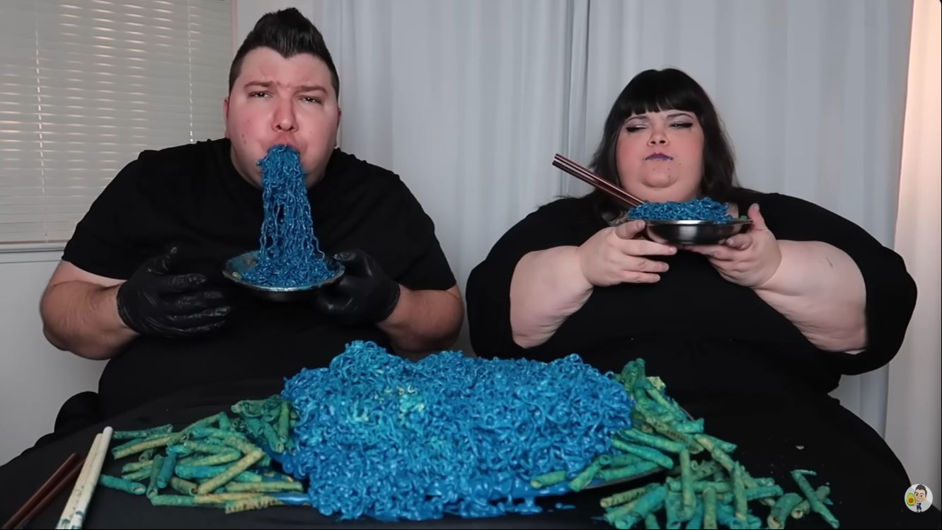 The same video also featured fellow creator Hungry Fat Chick as the pair shared an oversized spread of blue noodles and snacks, highlighting the collaborative eating challenges and larger-than-life mukbangs that became a hallmark of his channel. | Source: YouTube/Nikocado Avocado