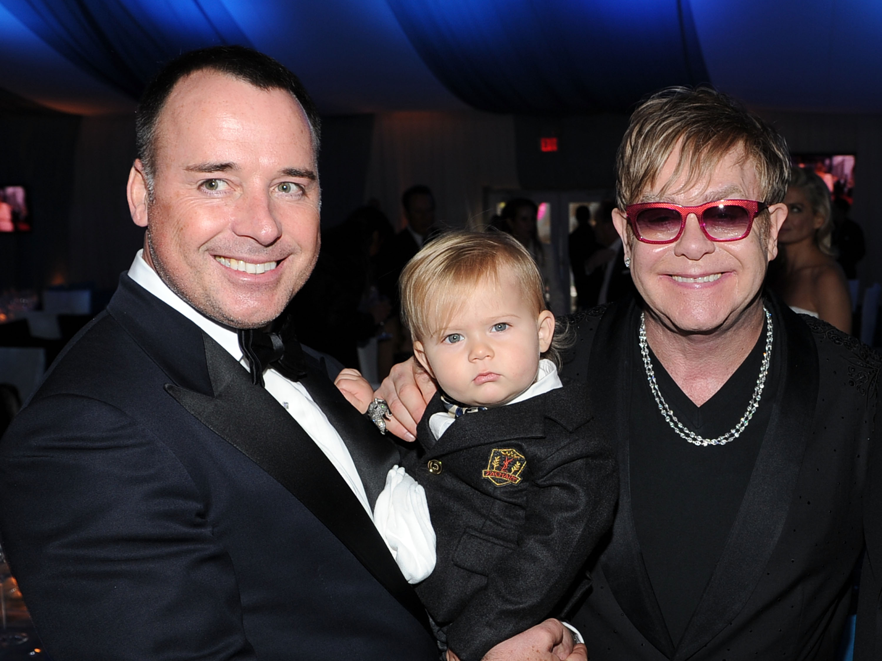 David Furnish and Sir Elton John arrived in polished black tie for the 20th Annual Elton John AIDS Foundation Academy Awards Viewing Party on February 26, 2012, in California, United States — but it was toddler Zachary John Furnish-John who quietly stole the spotlight. Dressed in a miniature suit with a crisp white shirt and tiny tie, the youngster was held between his fathers as they smiled for photographers.