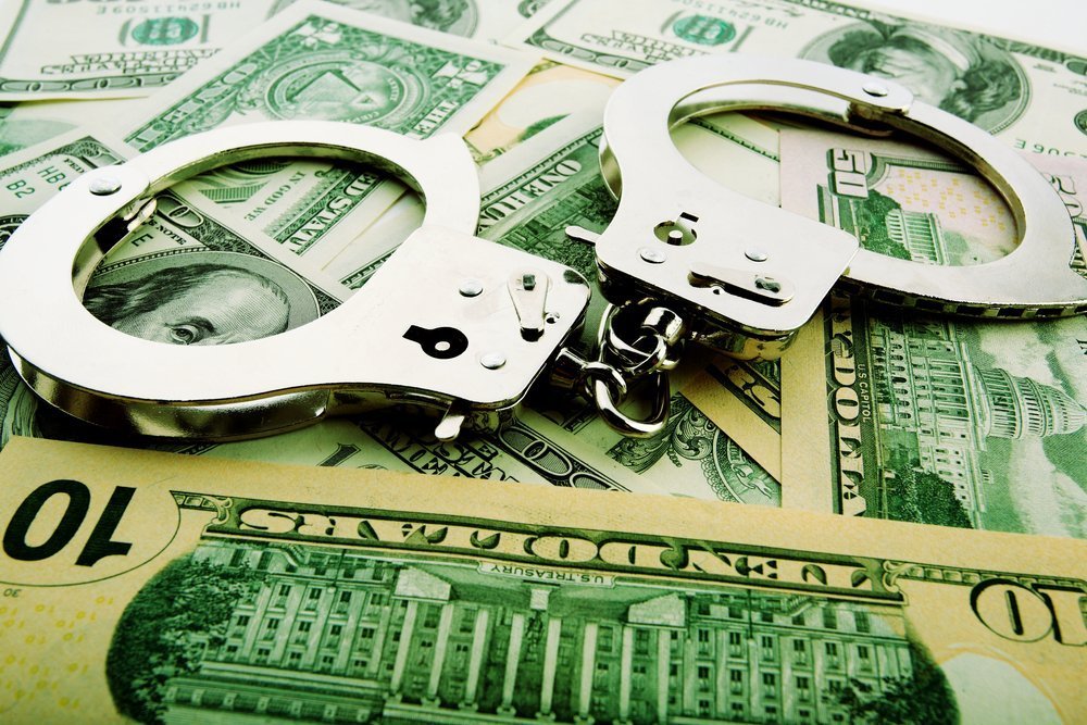Silver handcuff and dollar bank notes. | Photo: Shutterstock