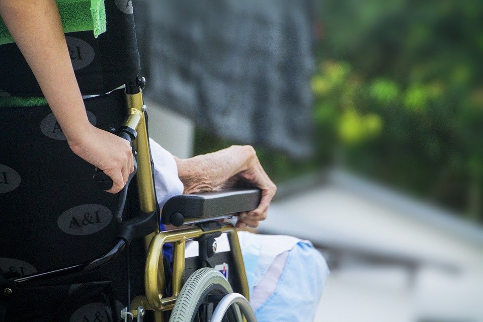 Anciana sobre silla de ruedas mientras es empujada por otra persona. | Imagen: Max Pixel