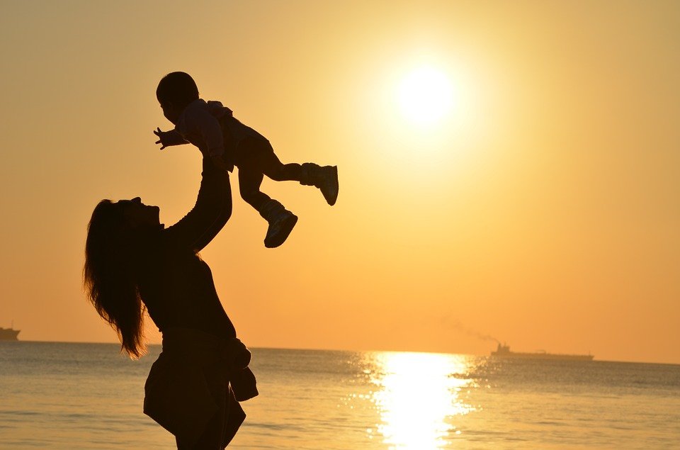A mother carrying her baby daughter into the sunset. | Photo: Pixabay