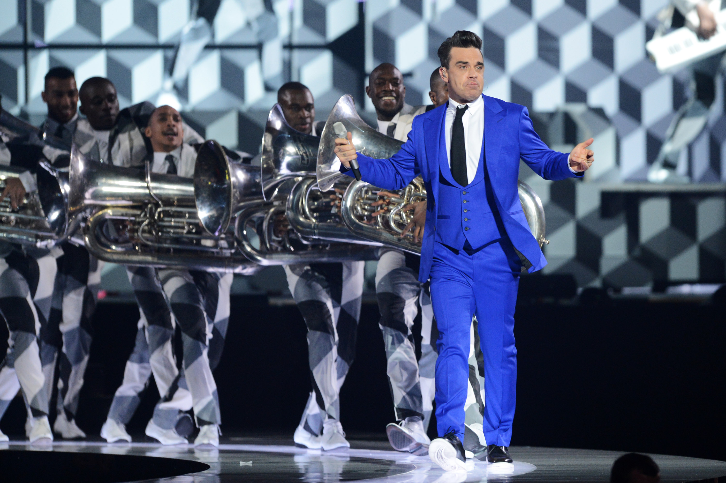 Robbie Williams performed at The Brit Awards 2013 on February 20 in London, England, wearing a striking electric-blue suit. Flanked by a brass band in bold black-and-white patterns, he delivered one of the night's most visually dynamic and energetic sets.