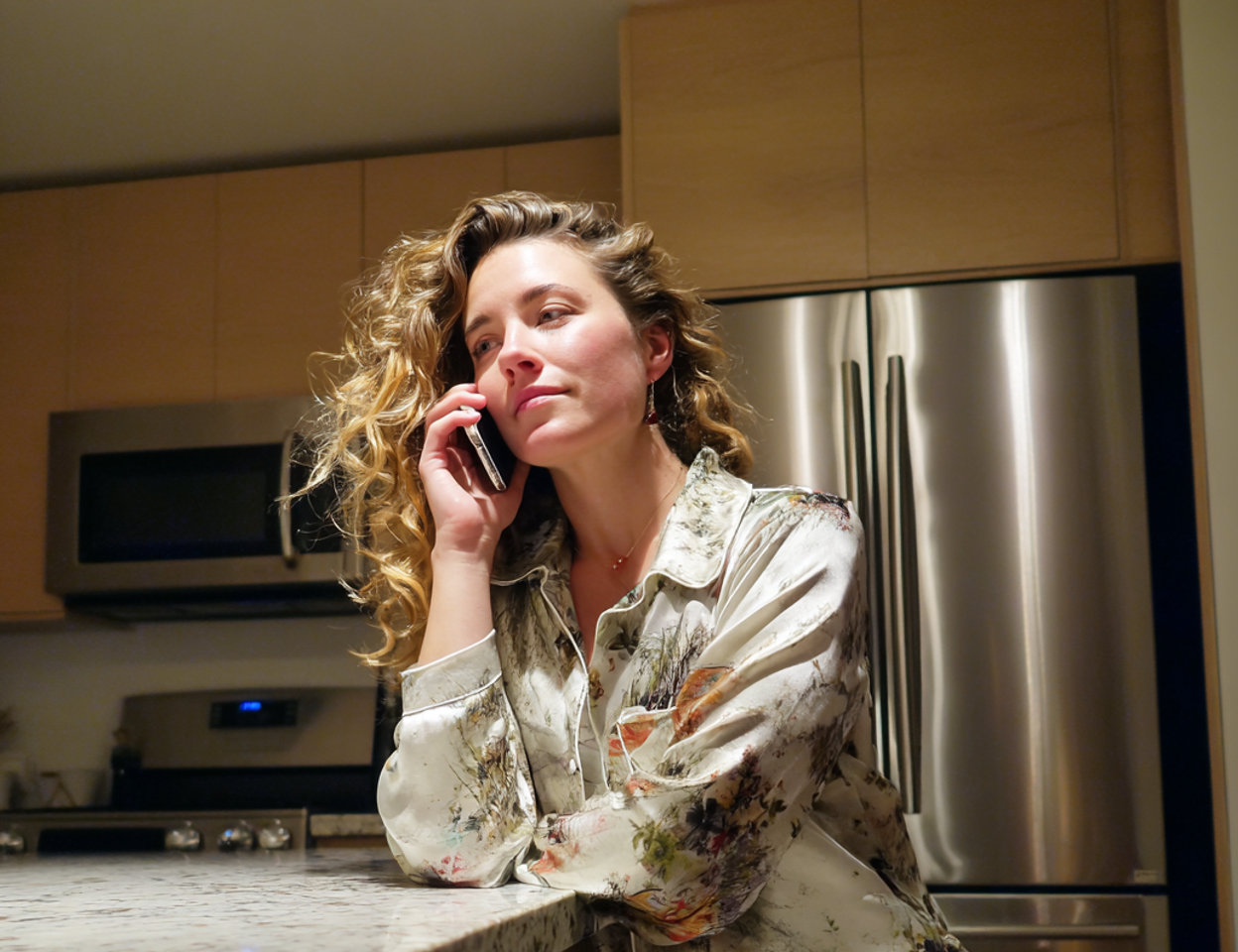 A woman sitting at a kitchen counter and talking on a phone | Source: Midjourney