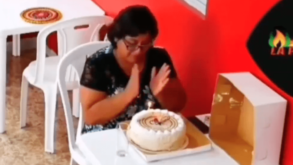 A woman sits at a table with a birthday cake in front of her and claps as she celebrates alone | Photo: Twitter/GoodNewsMoveme3