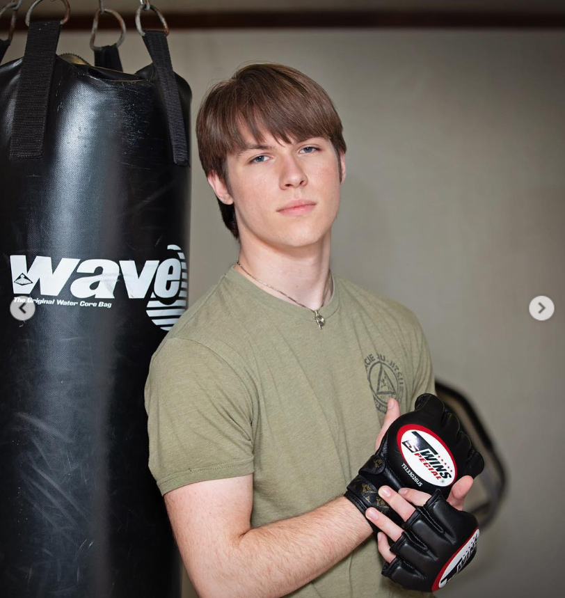 Dakota Norris stands poised beside a heavy punching bag, gloved hands ready, his calm expression hinting at quiet discipline. The gym setting frames him as focused and composed—strength held in reserve rather than on display. | Source: Instagram/d.ak.ot.a