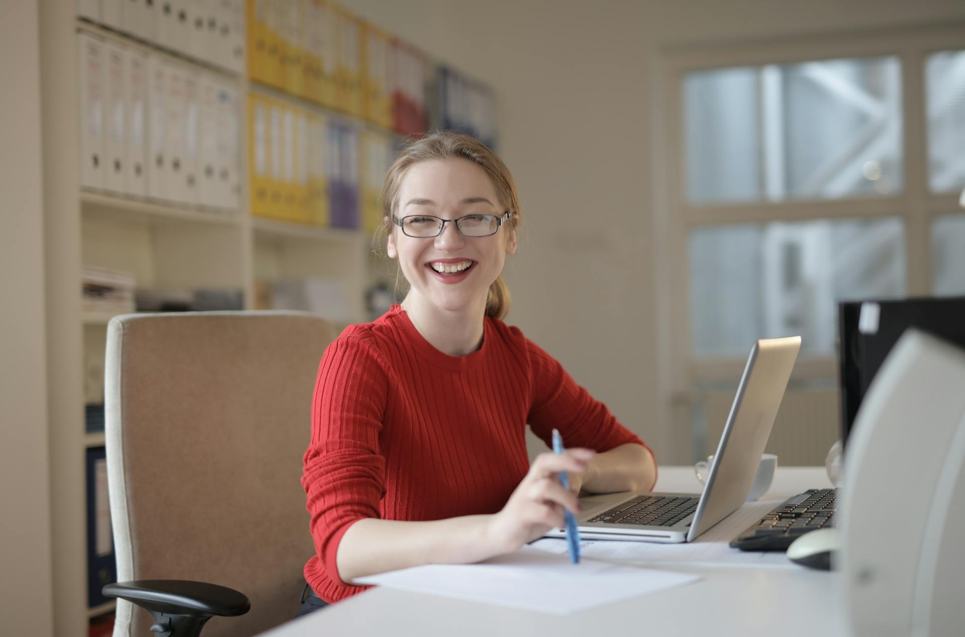 A woman in a red sweater leaning on a table while working | Source: Pexels