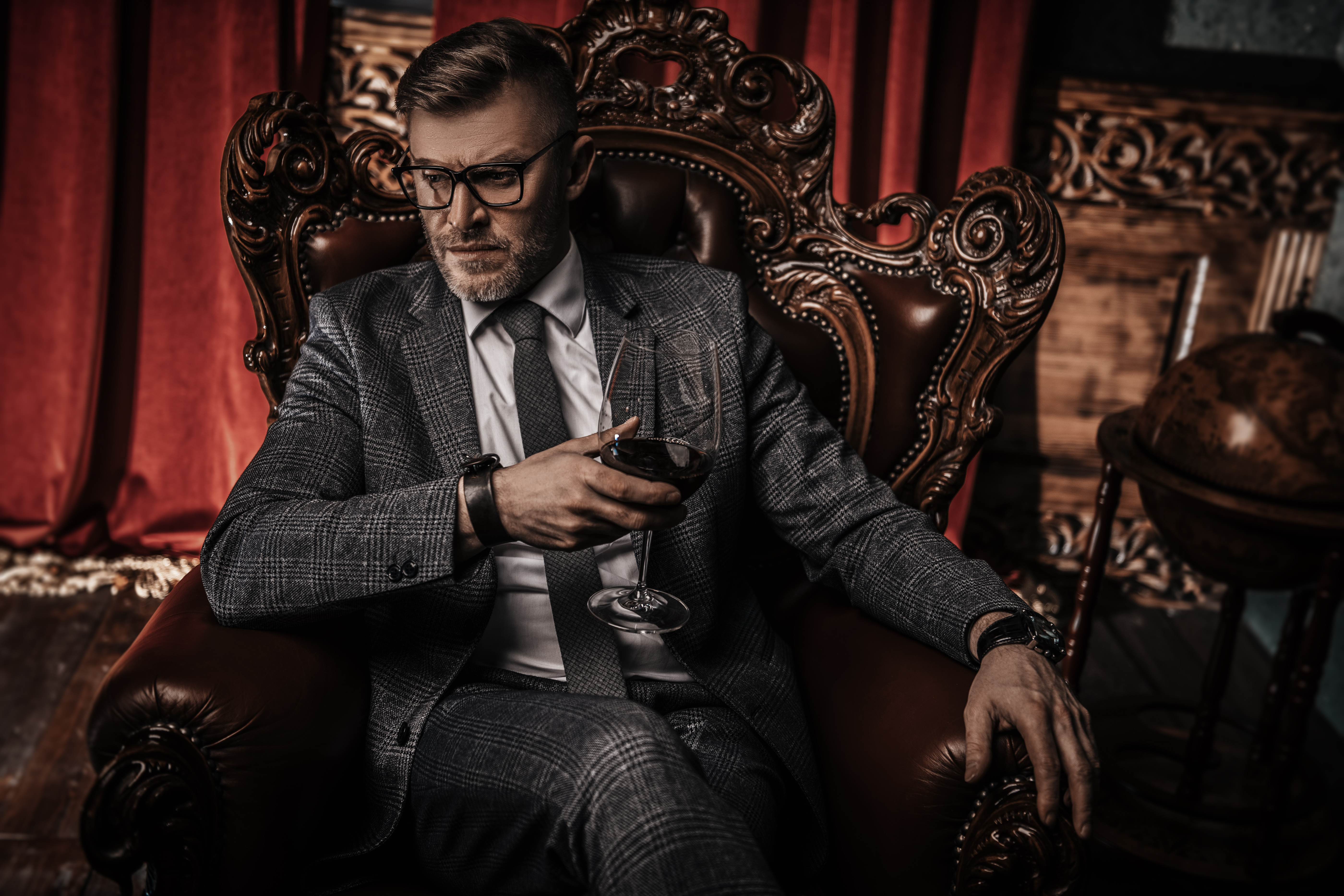 A portrait of a handsome mature man in a formal costume drinking wine in the armchair in the classic interior. | Source: Shutterstock