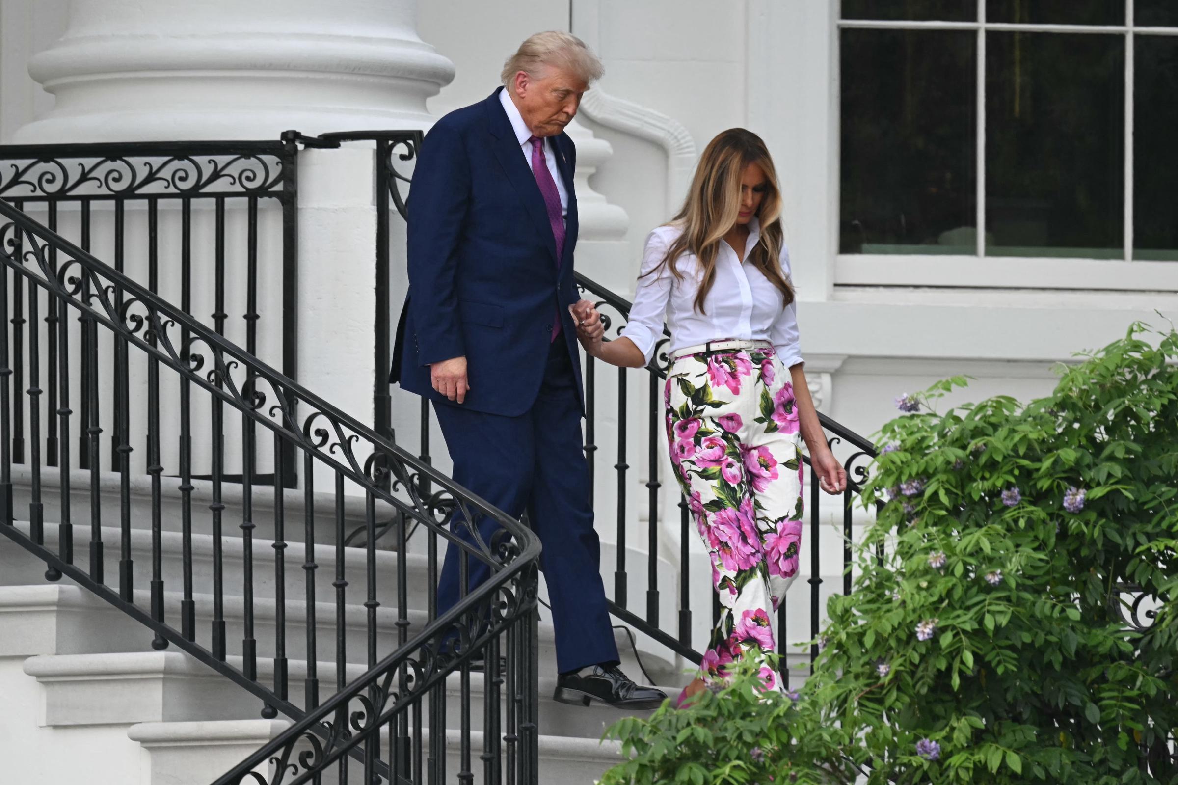 Donald and Melania Trump descend the White House steps hand-in-hand en route to the Congressional Picnic. Melania’s bright floral ensemble stands out against the classic architecture and leafy surroundings in this composed yet casual moment.