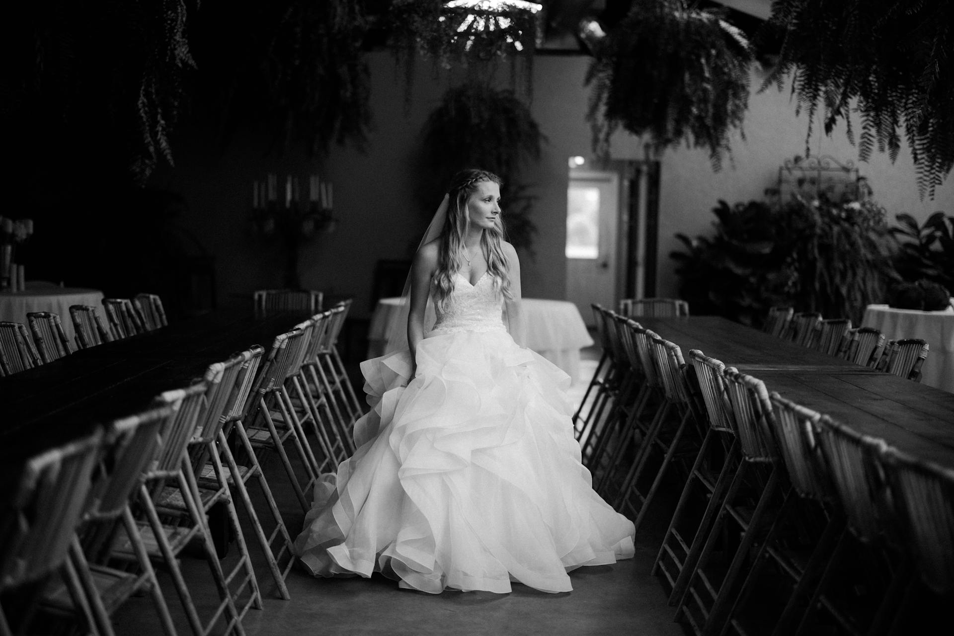 A grayscale photo of a bride standing walking down a row of empty chairs | Source: Pexels