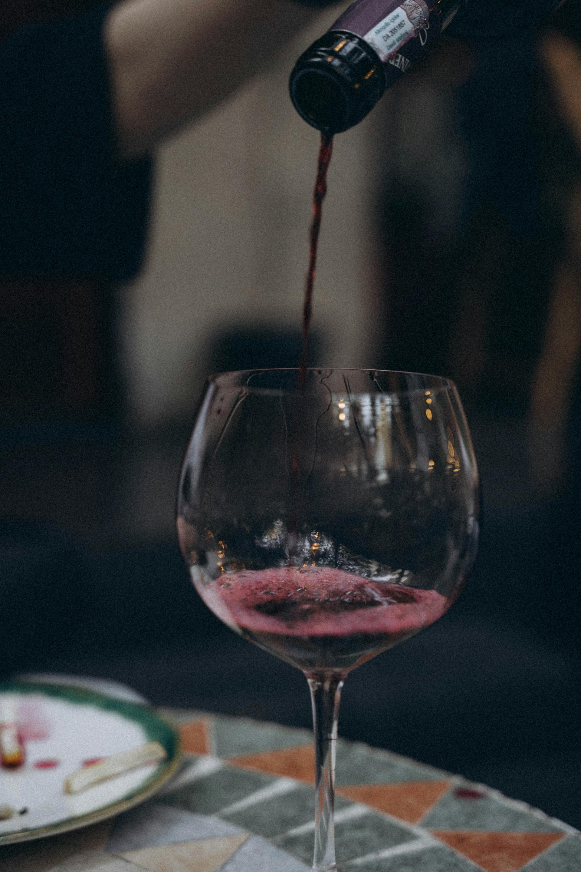 A closeup shot of a person pouring red wine into a glass | Source: Pexels