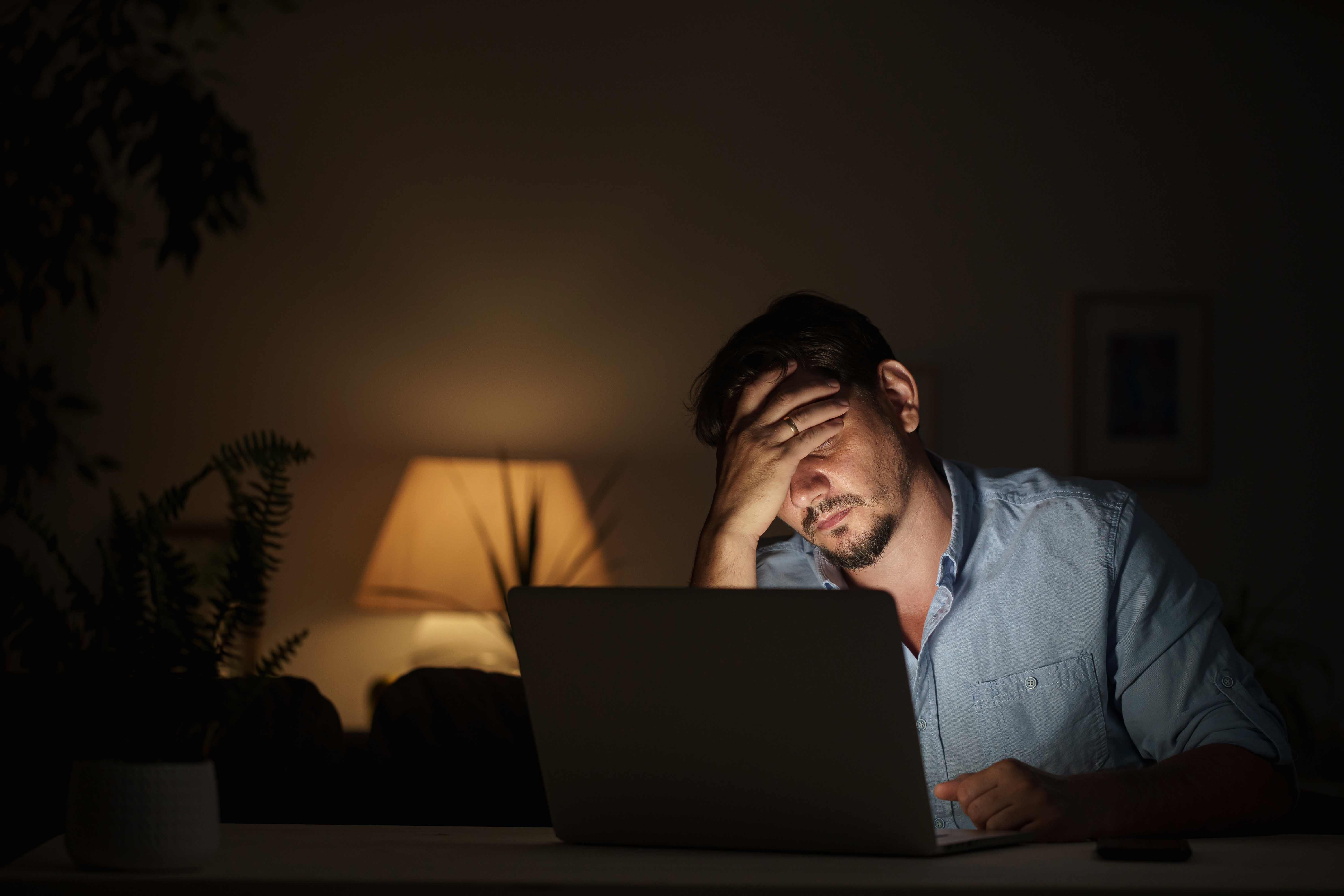 A man sitting in front of a laptop screen with his hand covering his eyes | Source: Shutterstock