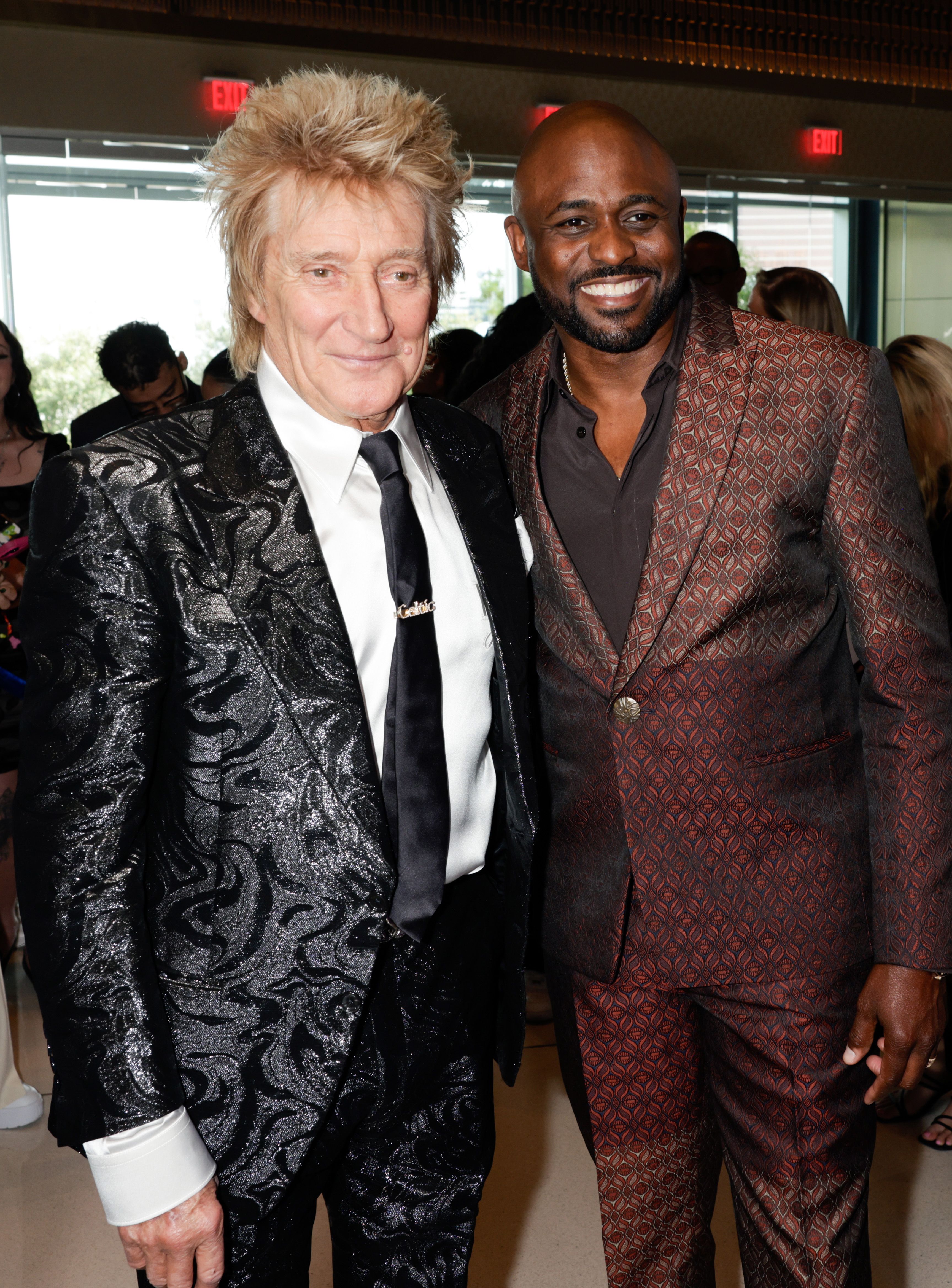 Rod poses with Wayne Brady before the AMAs, both beaming in sharp suits. Rod’s black, swirling patterned tux catches the light, while Wayne goes for a rich, textured burgundy ensemble. Their styles clash perfectly — classic meets contemporary — just ahead of a night full of music and celebration.