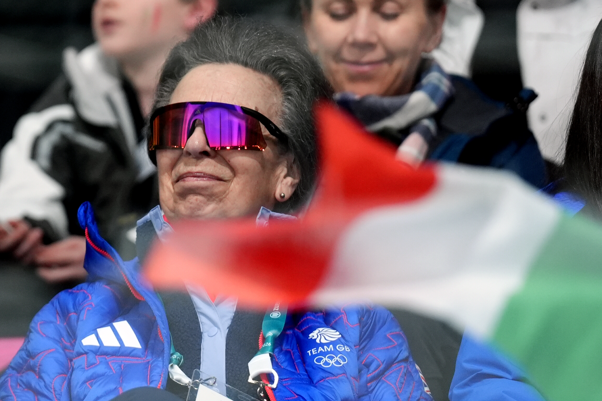 The Princess Royal watched the Curling Mixed Doubles Bronze Medal Game at the Cortina Curling Olympic Stadium on February 10, 2026, her mirrored sunglasses reflecting the bright arena lights as an Italian flag blurred across the foreground. Wrapped in a vivid Team GB jacket with accreditation lanyard in place, she appeared quietly intent on the ice.