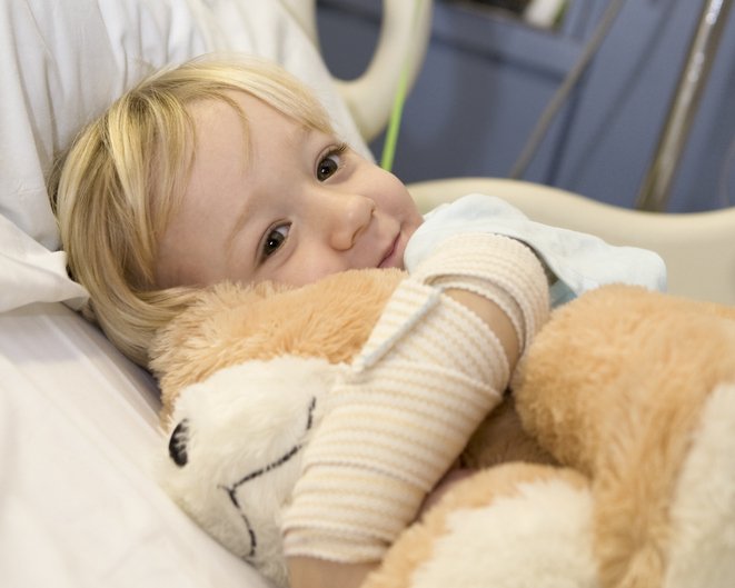 Kleines Kleinkind, umarmt seinen Teddybär und lächelt, als er in einem Krankenhausbett liegt. I Quelle: Getty Images
