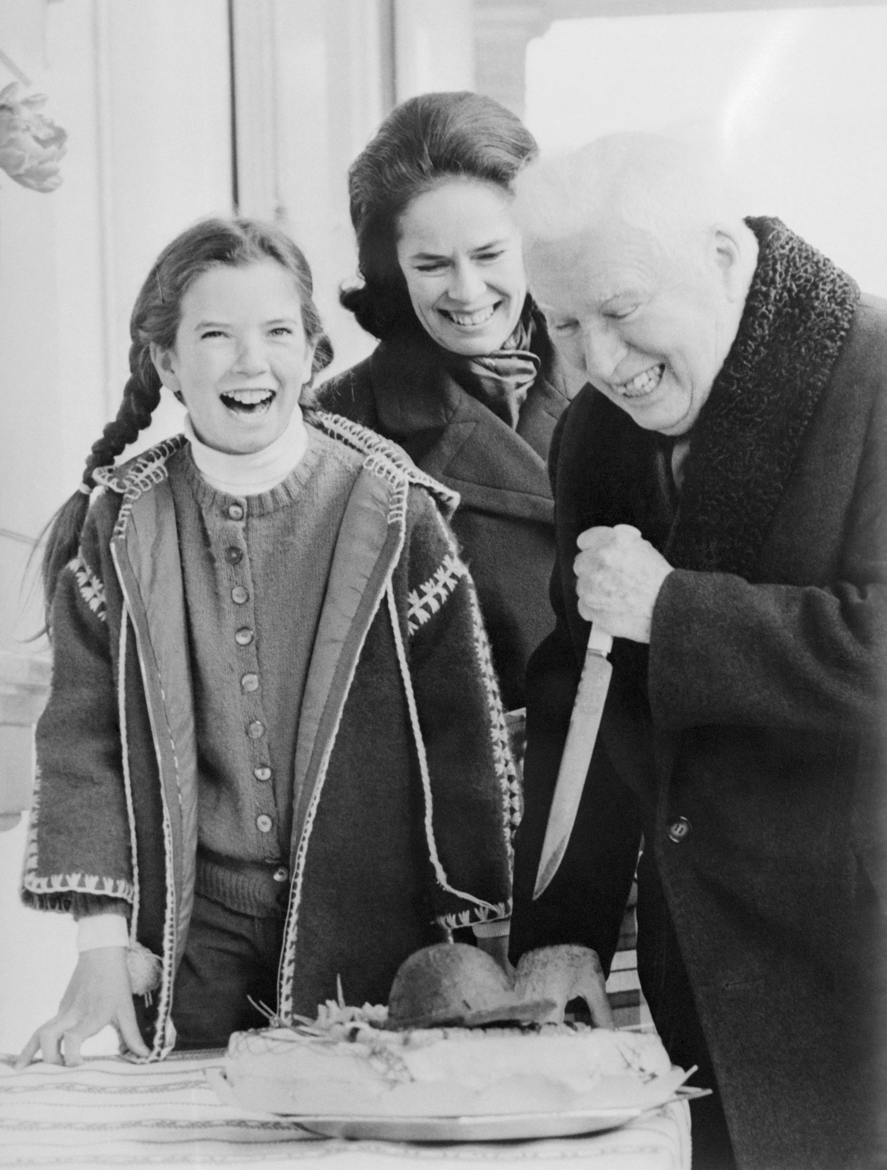 Charles Chaplin gets some help from his wife, Oona, and their daughter, Jane, as he cuts his 80th birthday cake at his home in Vevey, Switzerland, on April 16, 1969. | Source: Getty Images