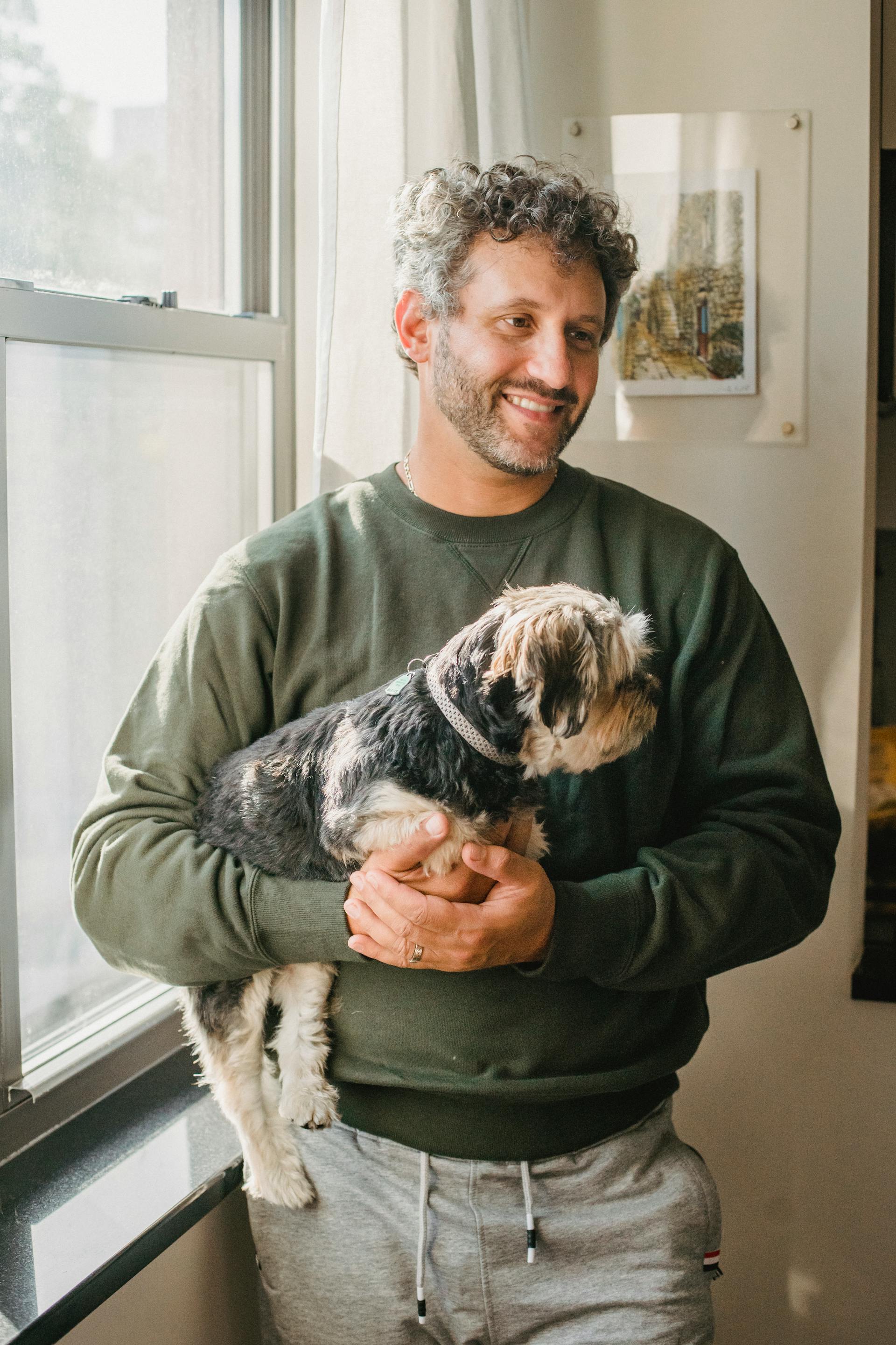 A man holding a dog while standing near a window | Source: Pexels